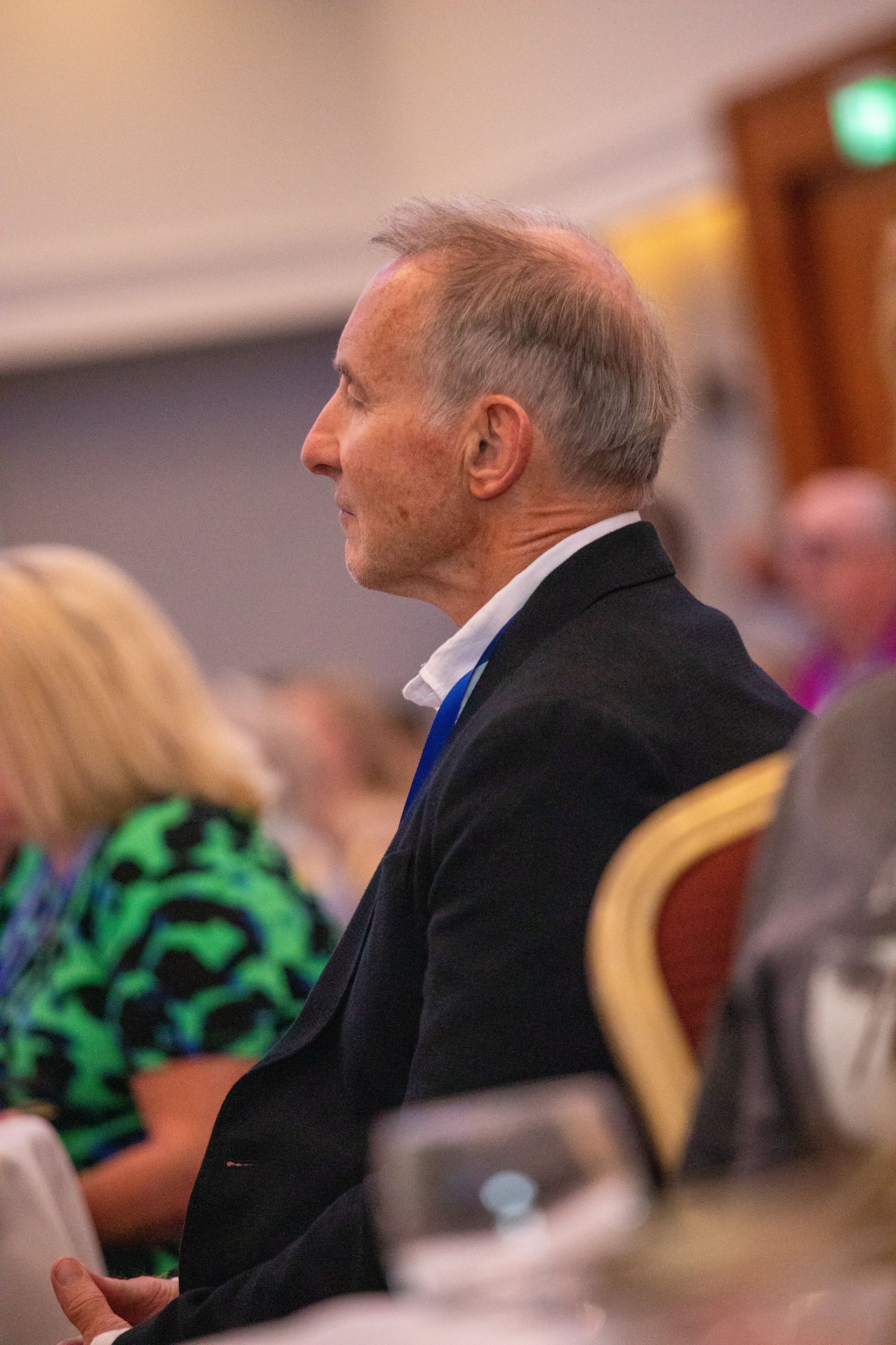 A man in a suit and tie is sitting at a table with other people.