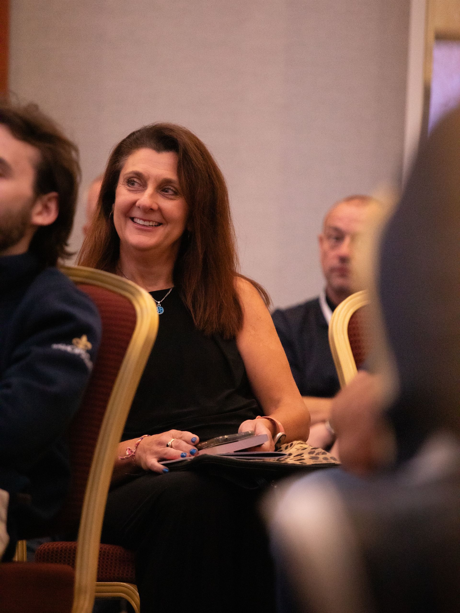 A woman is smiling while sitting in a chair at a conference.