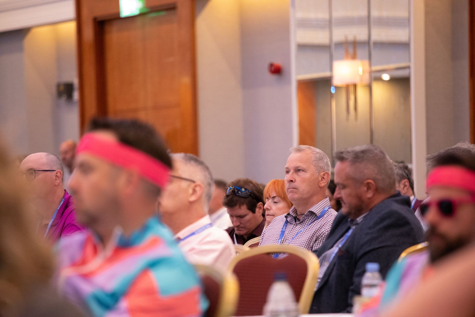 A group of people are sitting in a room wearing pink headbands.