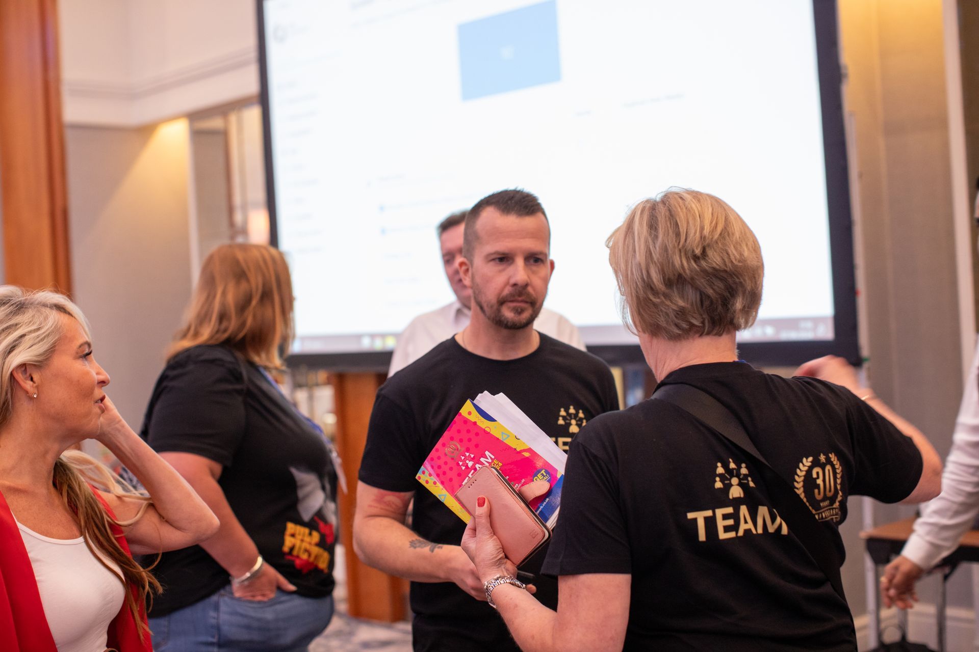 A group of people are standing in a room talking to each other.