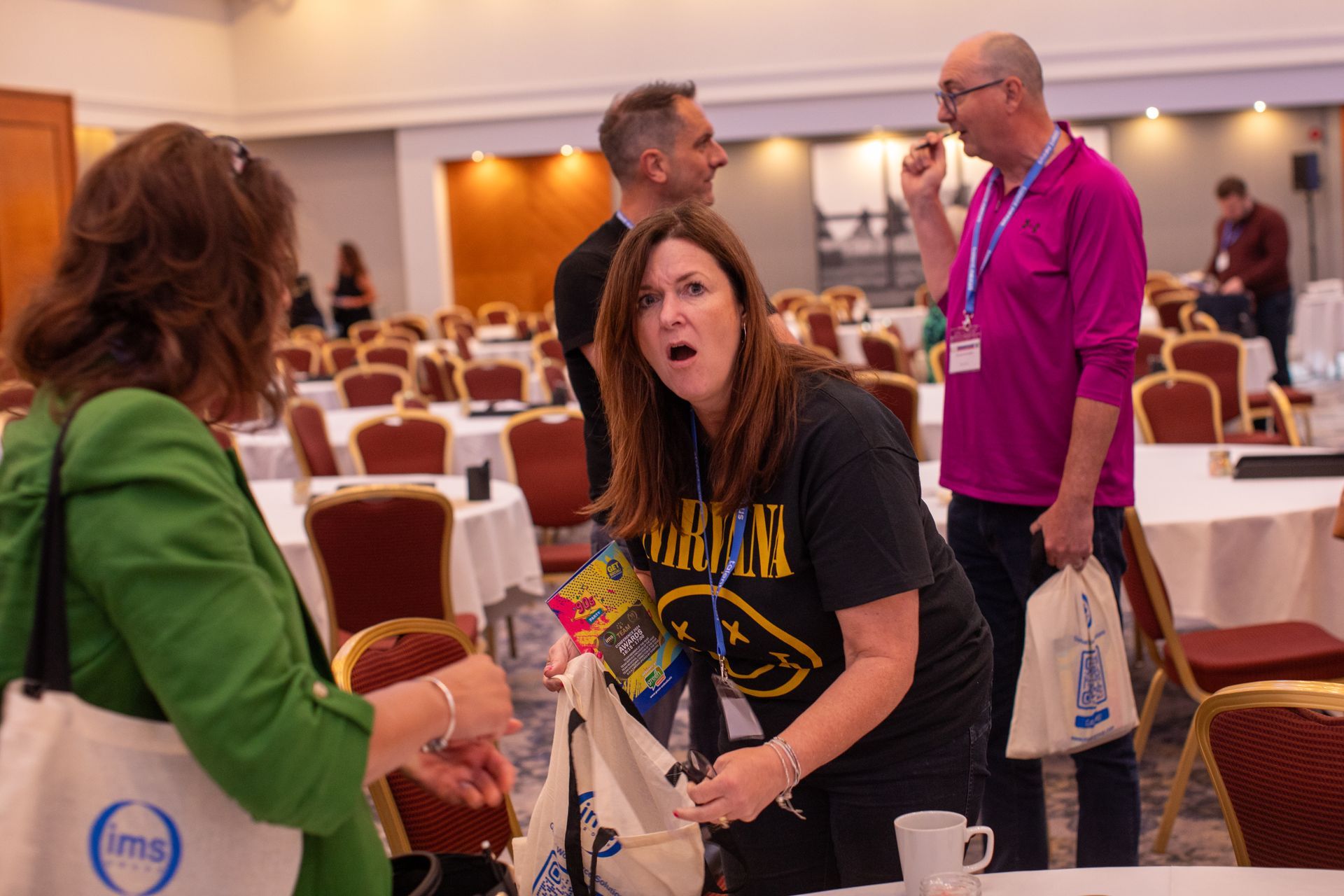 A group of people are standing around tables in a room talking to each other.