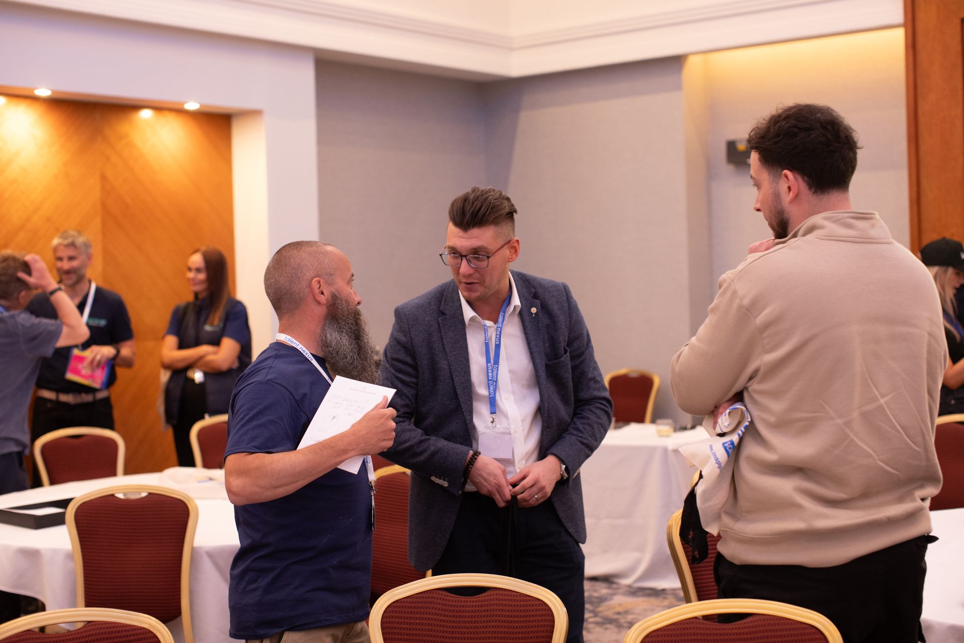A group of men are standing in a room talking to each other.