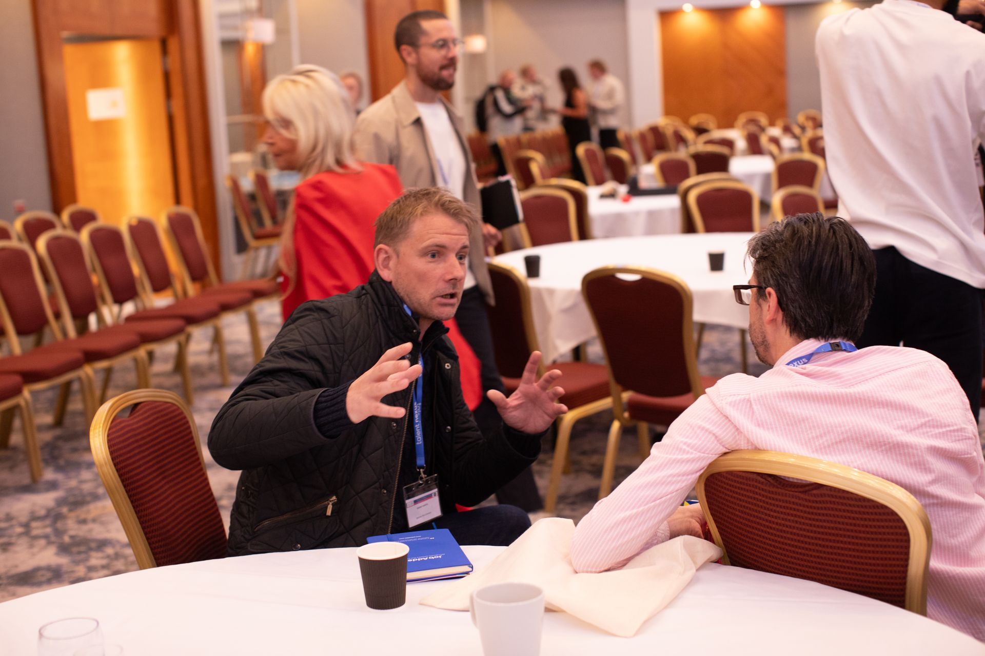 Two men are sitting at a table talking to each other in a conference room.