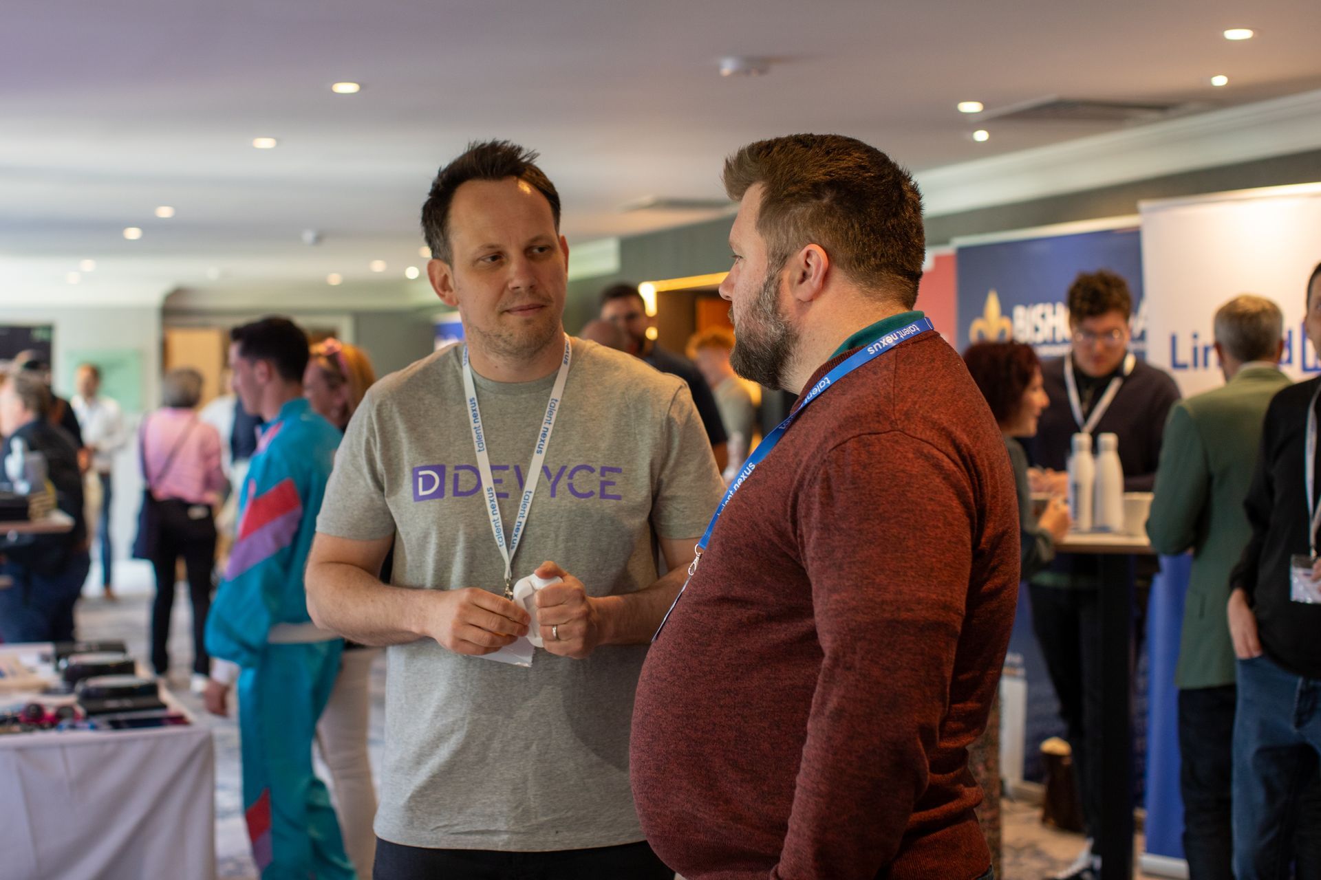 Two men are standing next to each other in a room talking to each other.