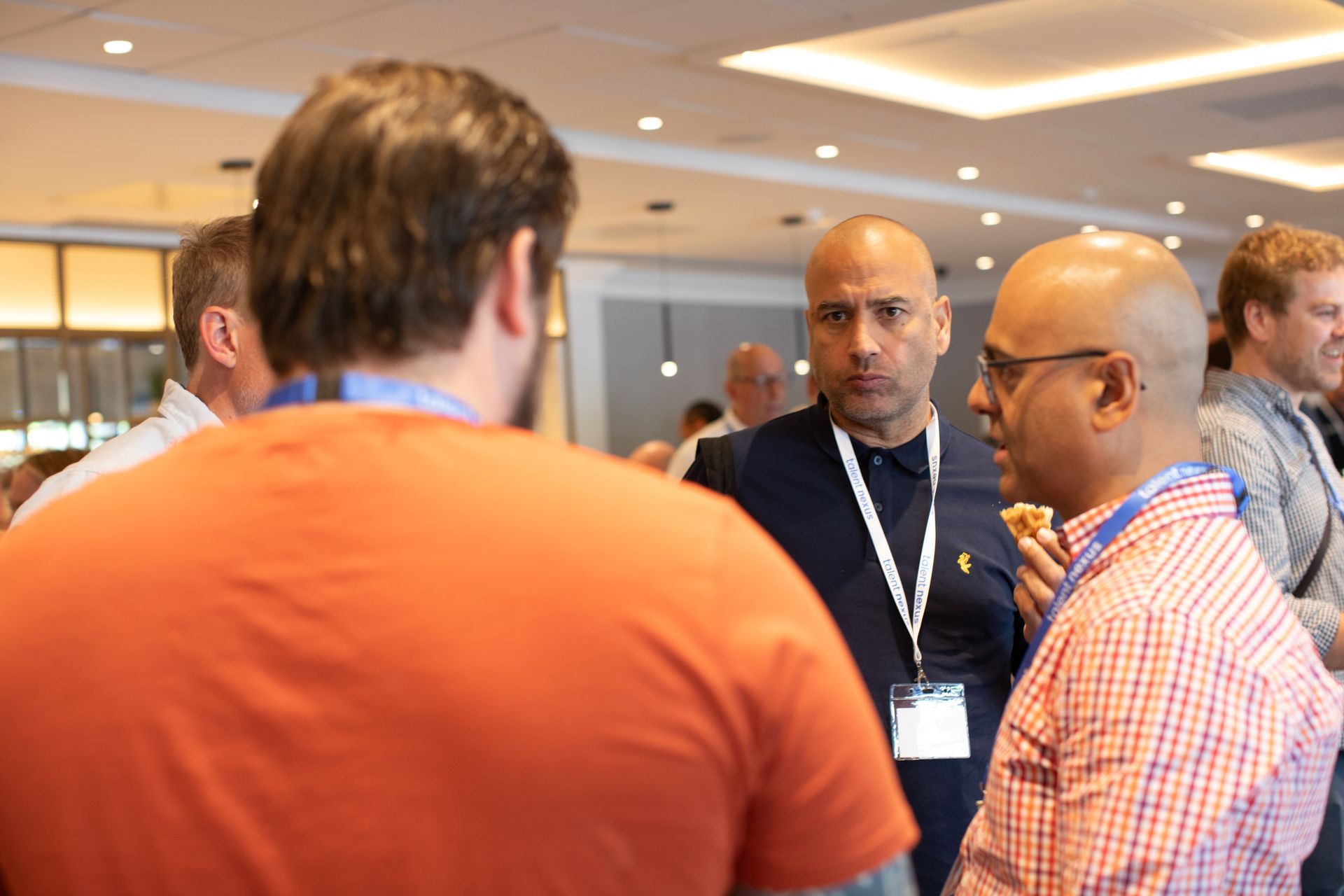 A group of men are standing in a room talking to each other.