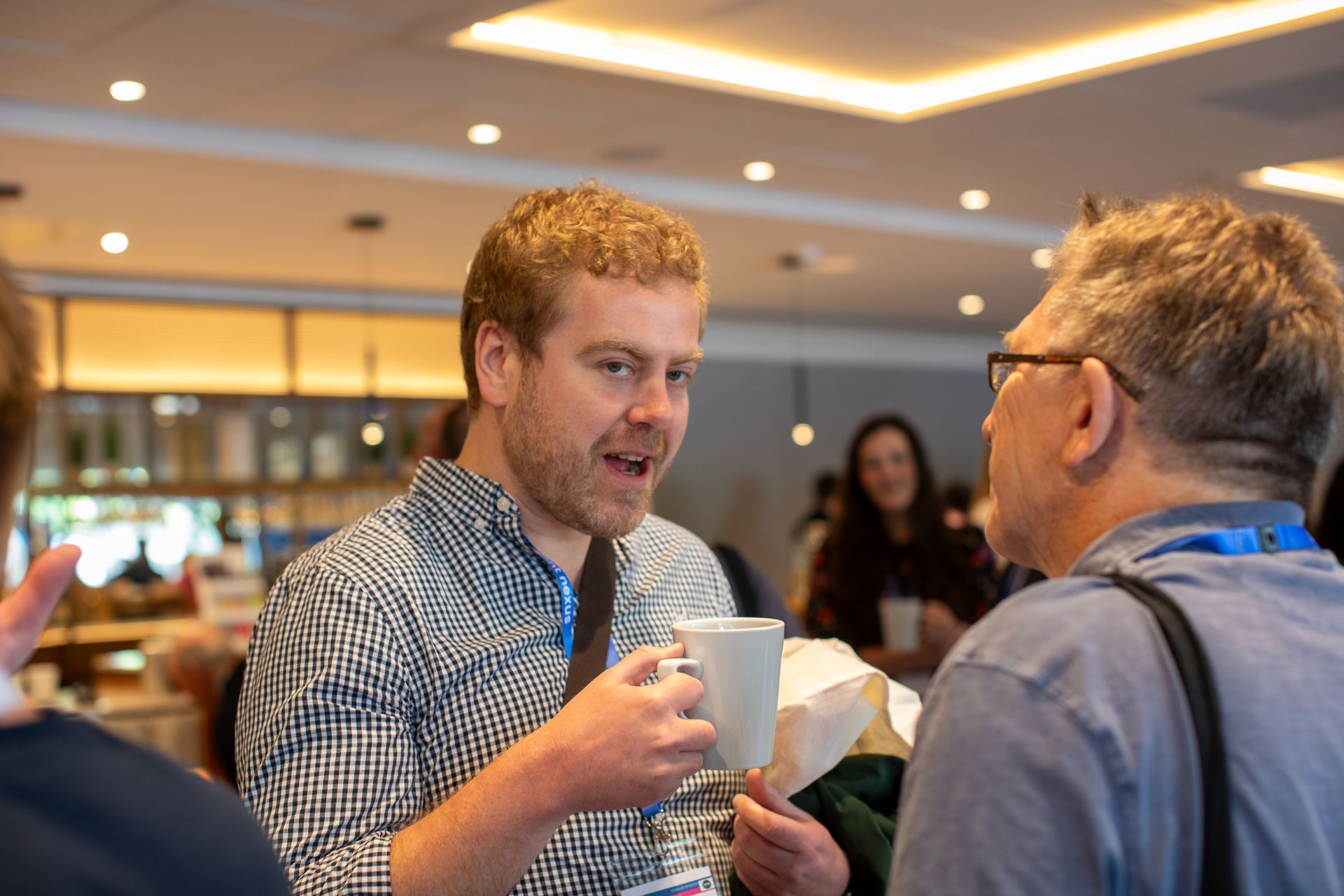 A man is holding a cup of coffee and talking to another man.