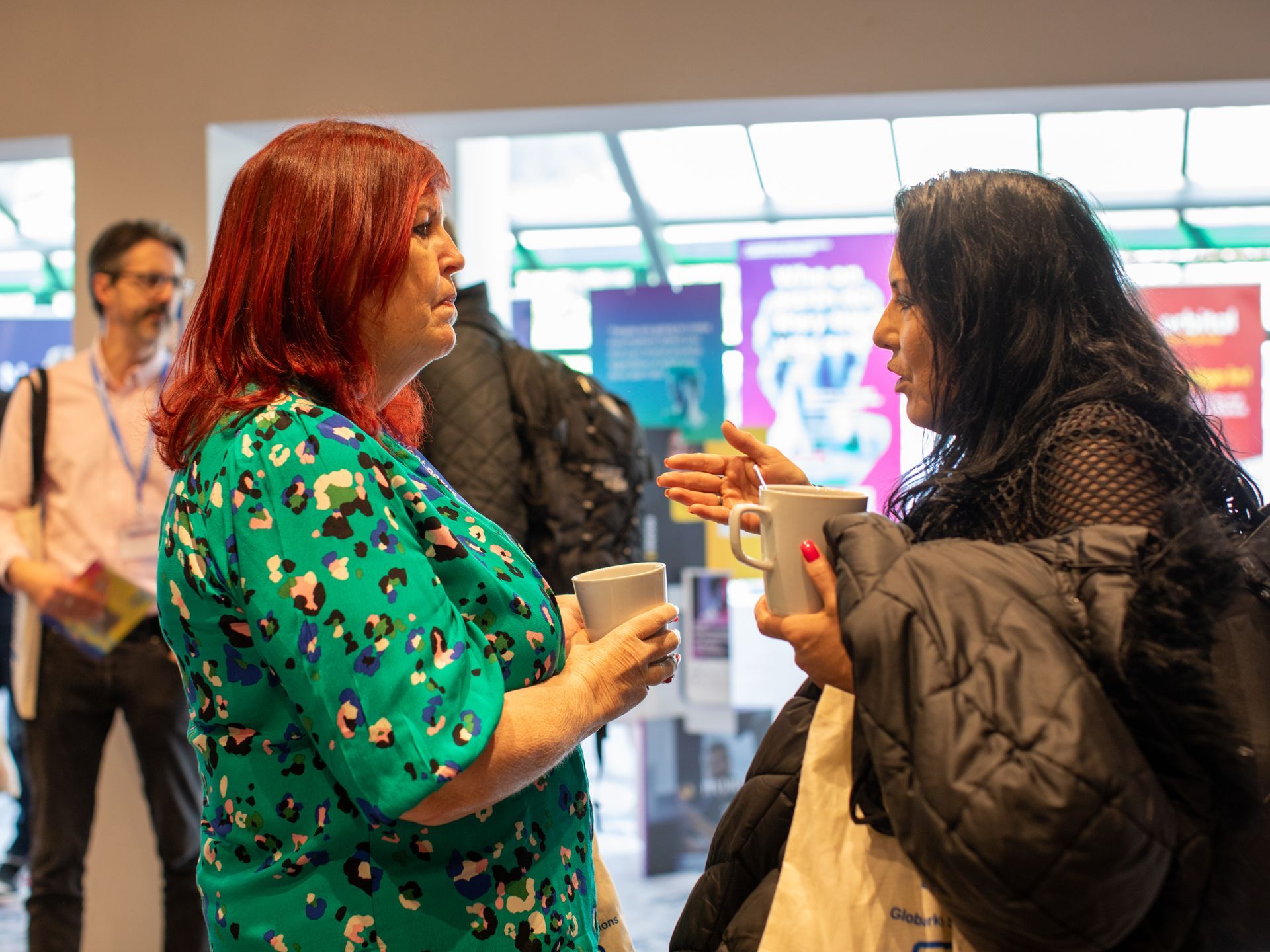 Two women are talking to each other while holding cups of coffee.
