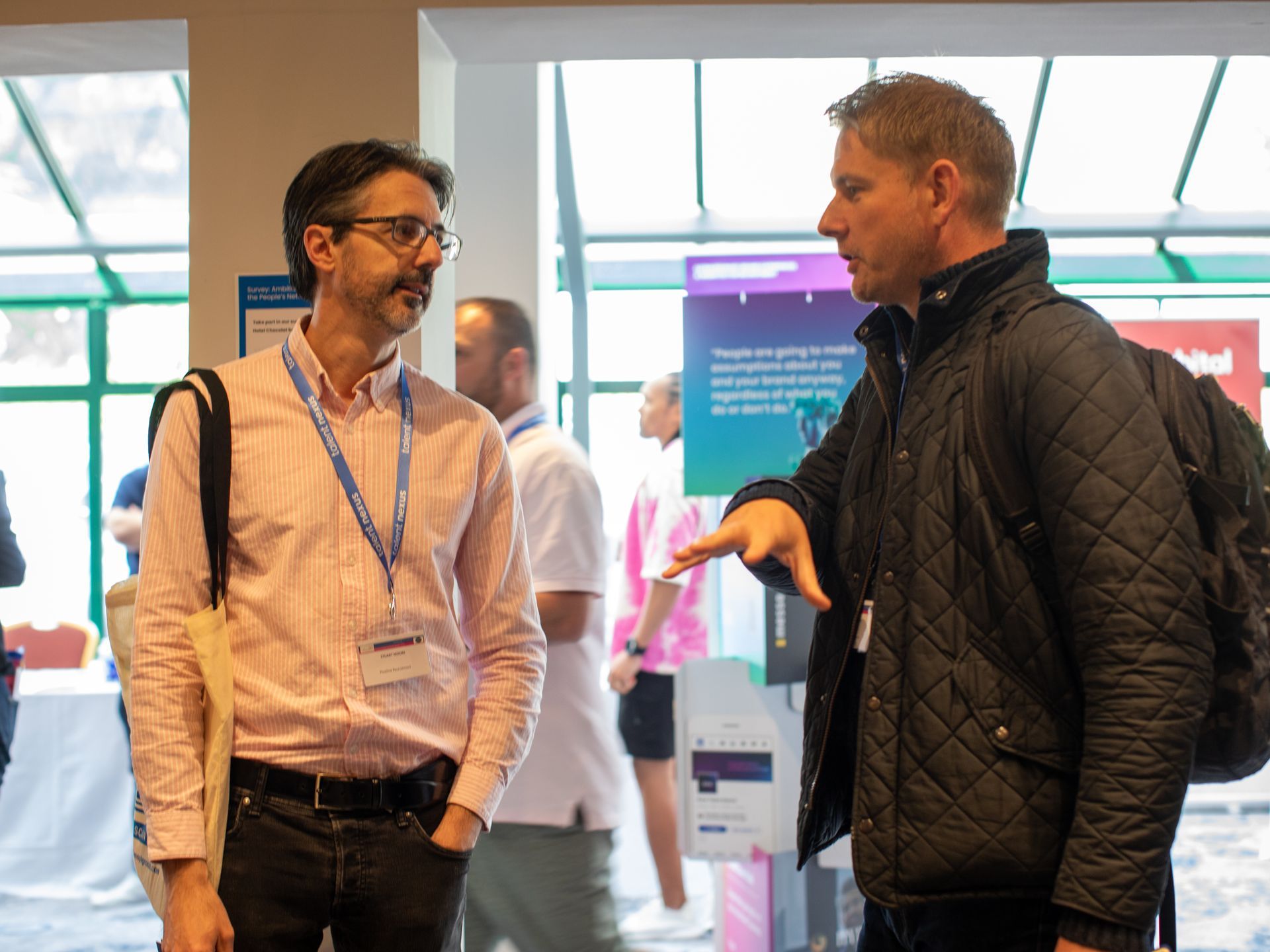 Two men are standing next to each other and talking in a room.