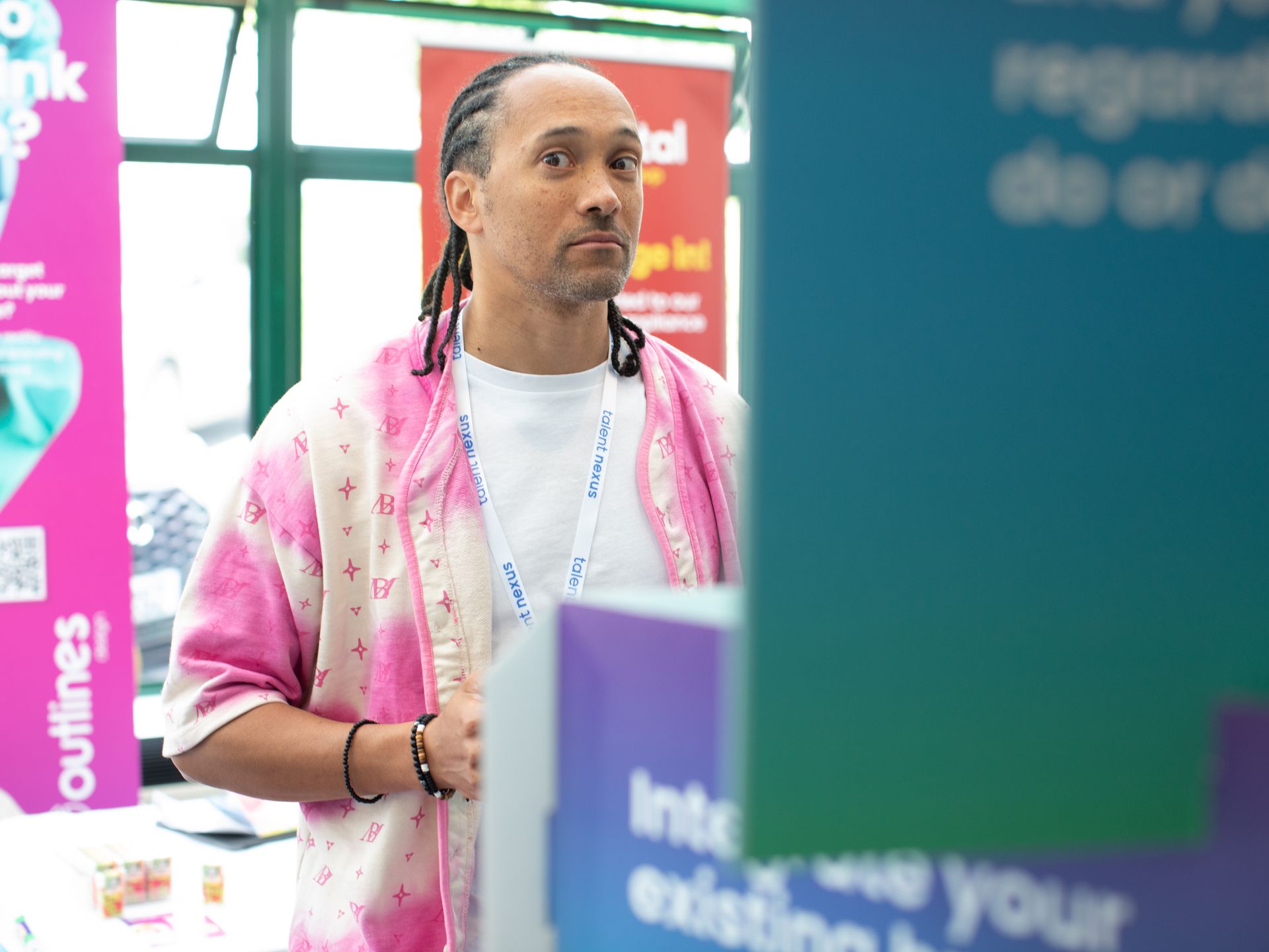 A man with dreadlocks is standing in front of a pink and blue sign.