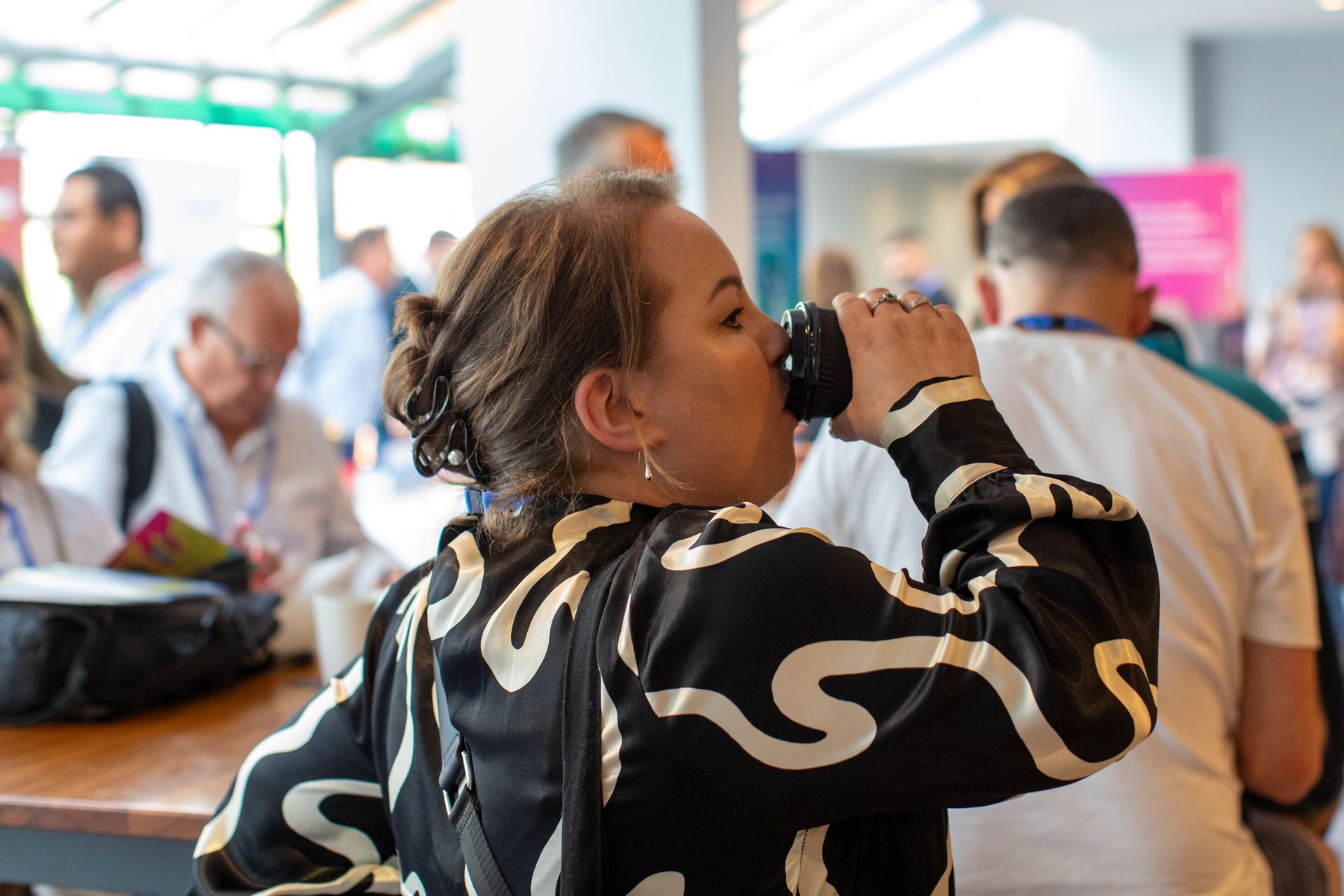 A woman is drinking from a cup while sitting at a table.