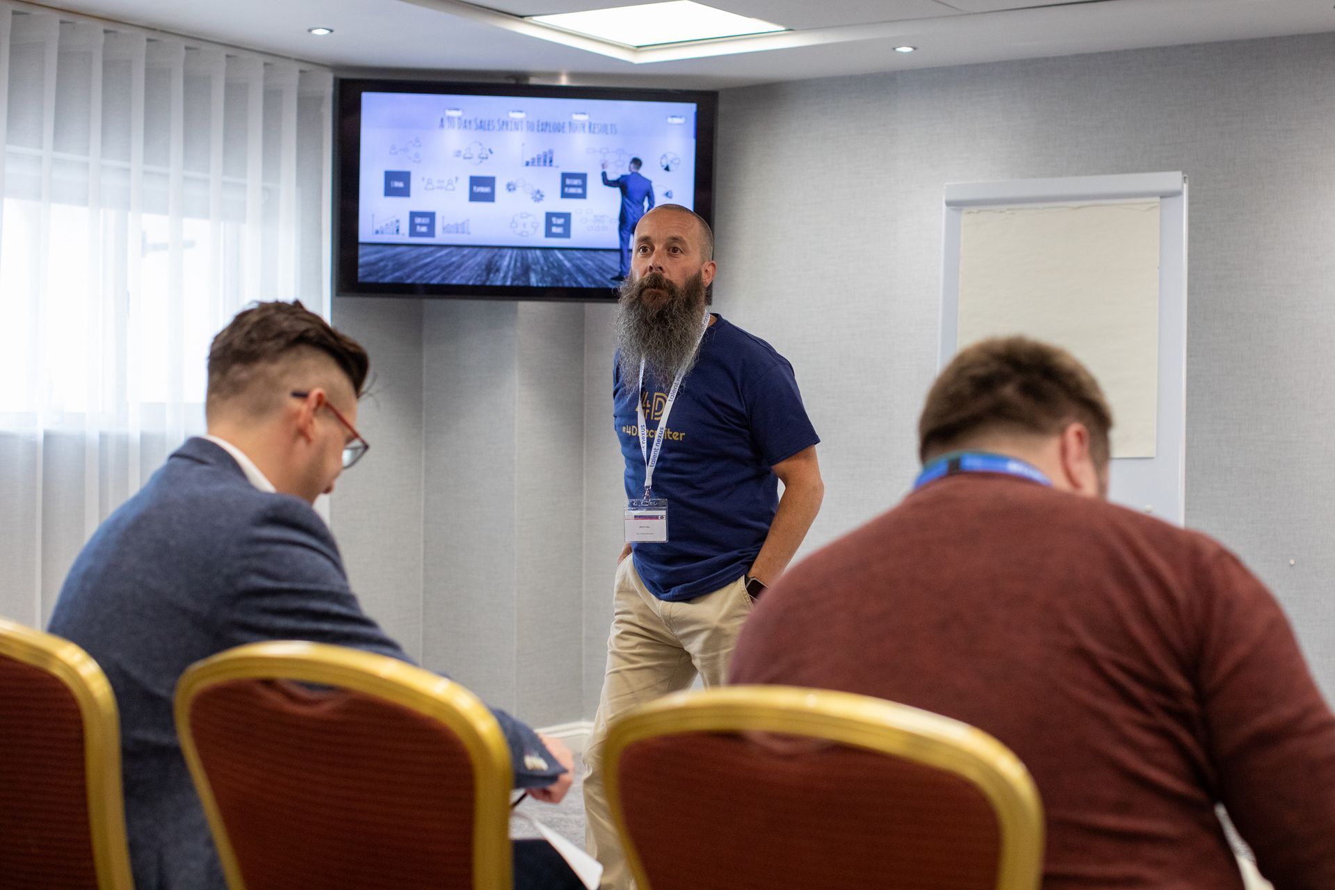 A man with a beard is giving a presentation to a group of people in a conference room.