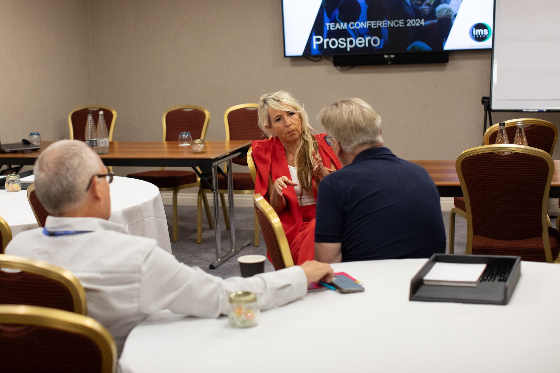A group of people are sitting at tables in a conference room talking to each other.
