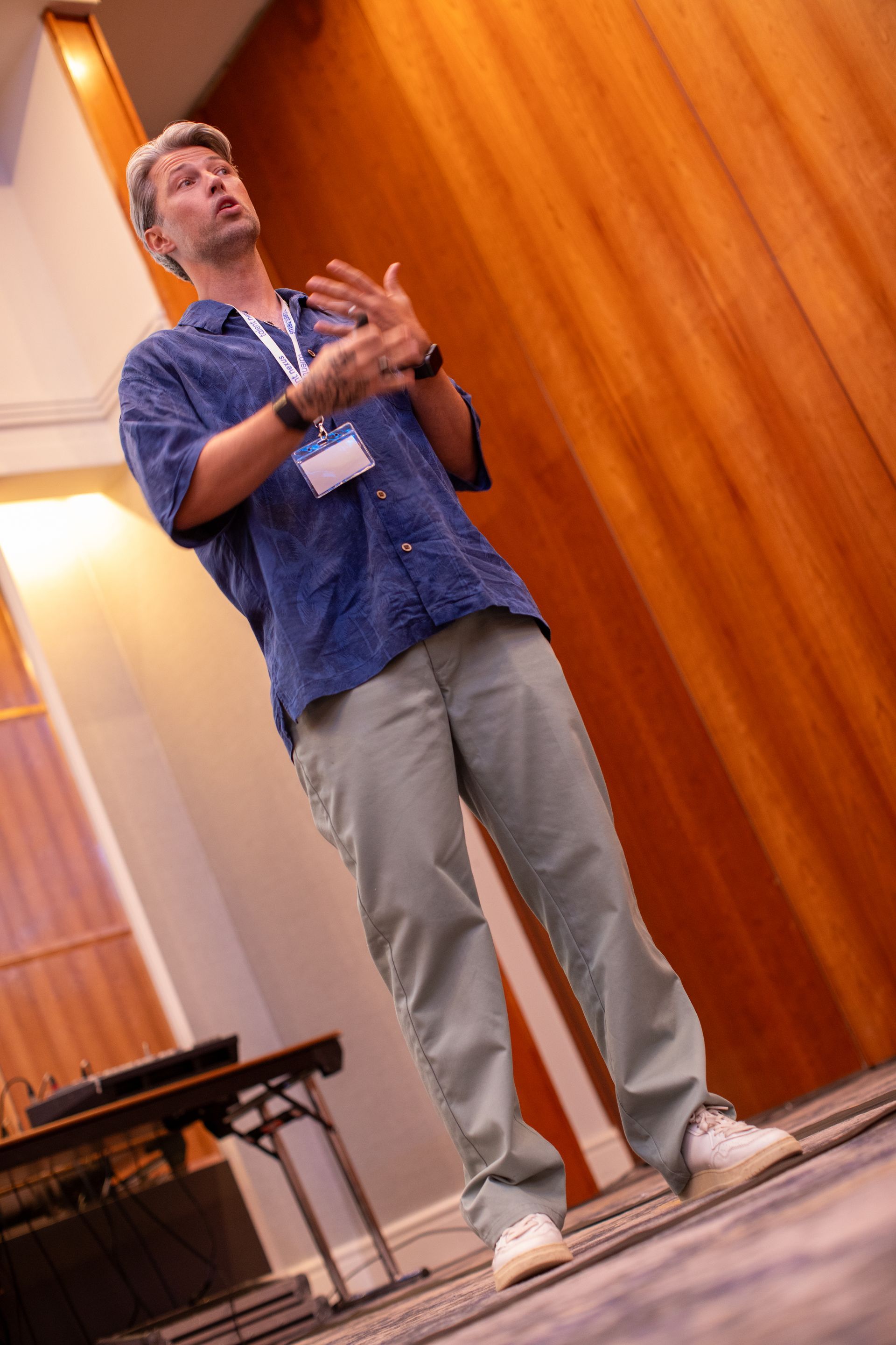 A man wearing a name tag is standing in front of a wooden wall