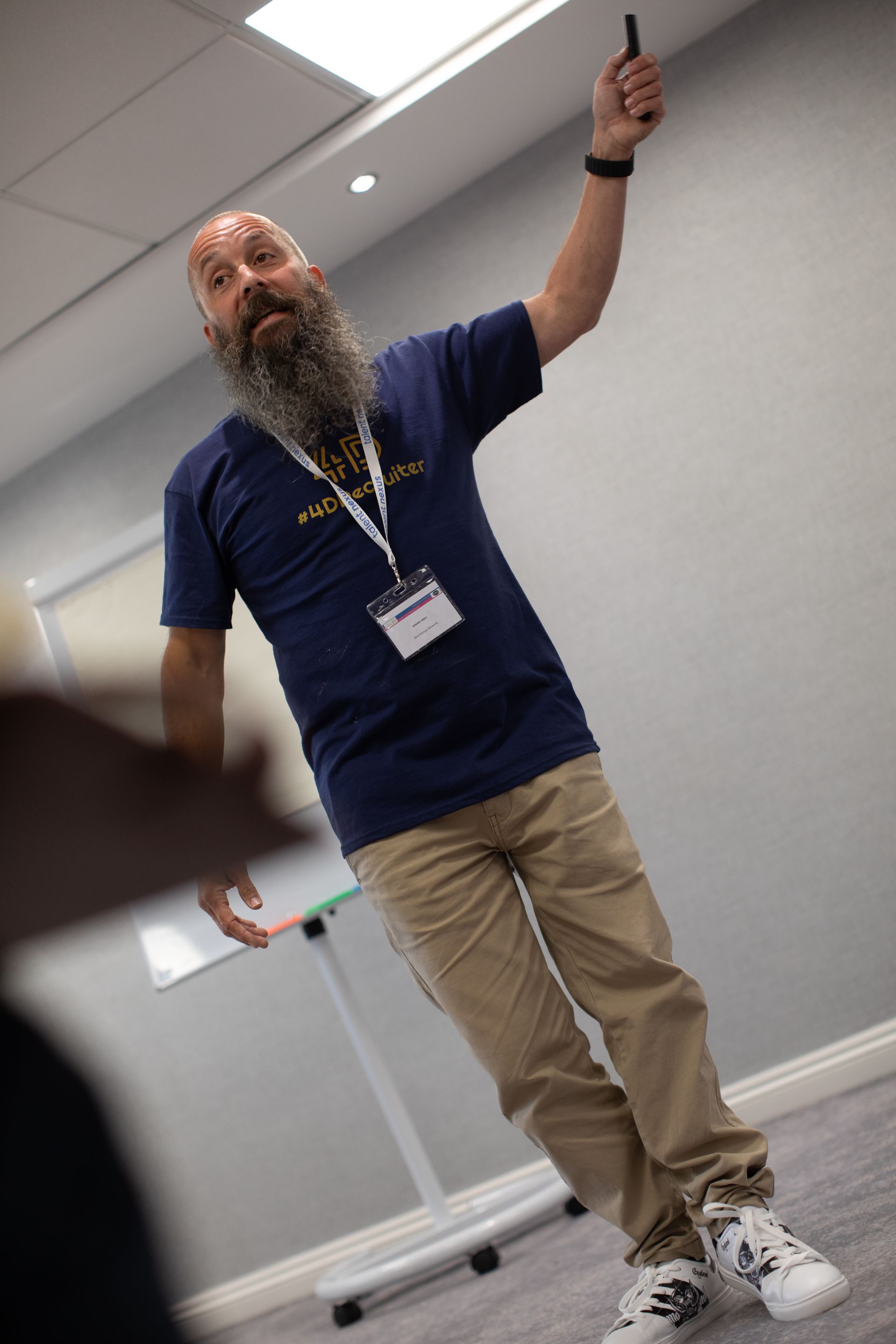 A man with a beard is standing in a room holding a pen.