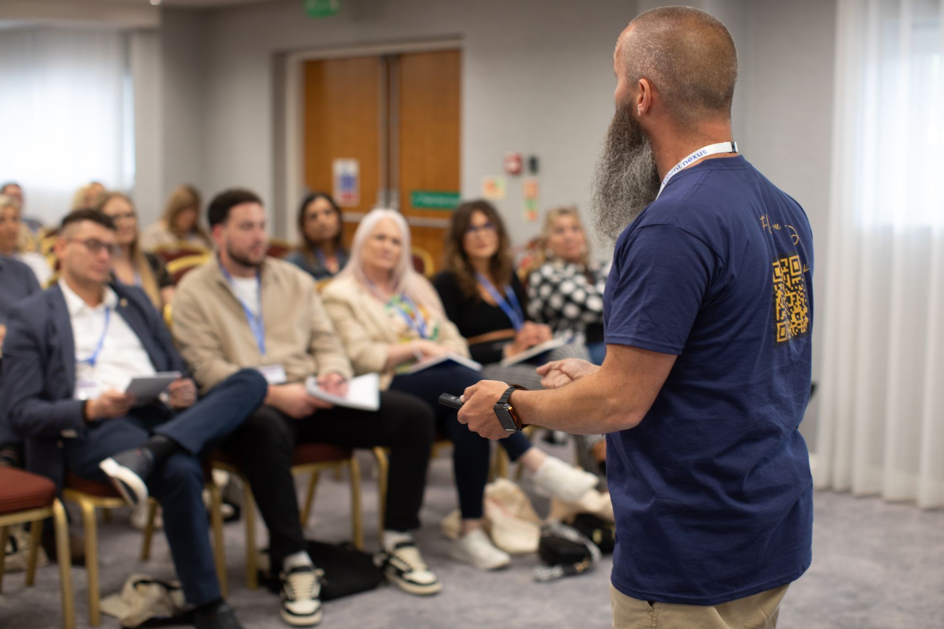 A man with a beard is giving a presentation to a group of people sitting in chairs.
