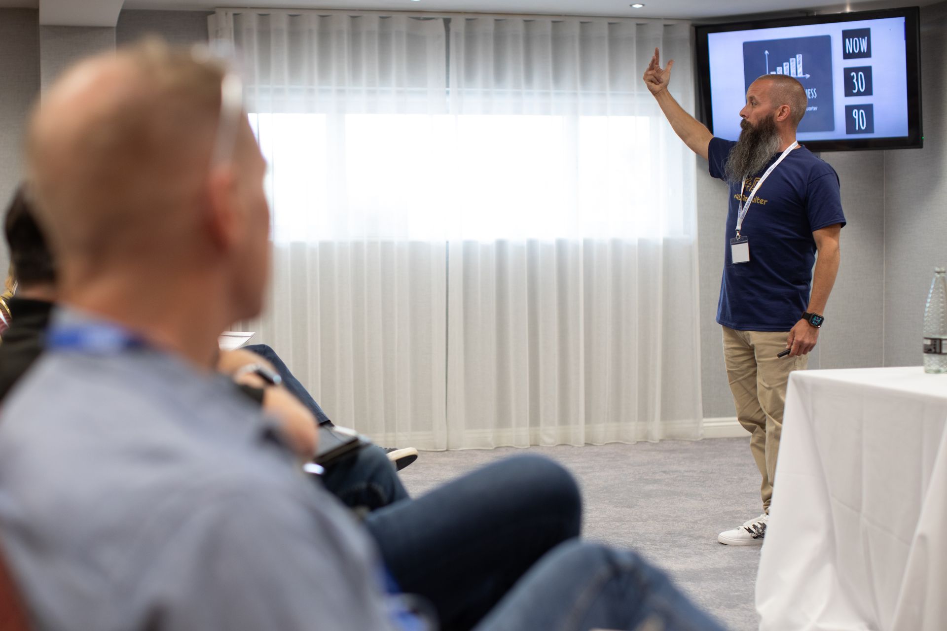 A man with a beard is giving a presentation in front of a group of people.