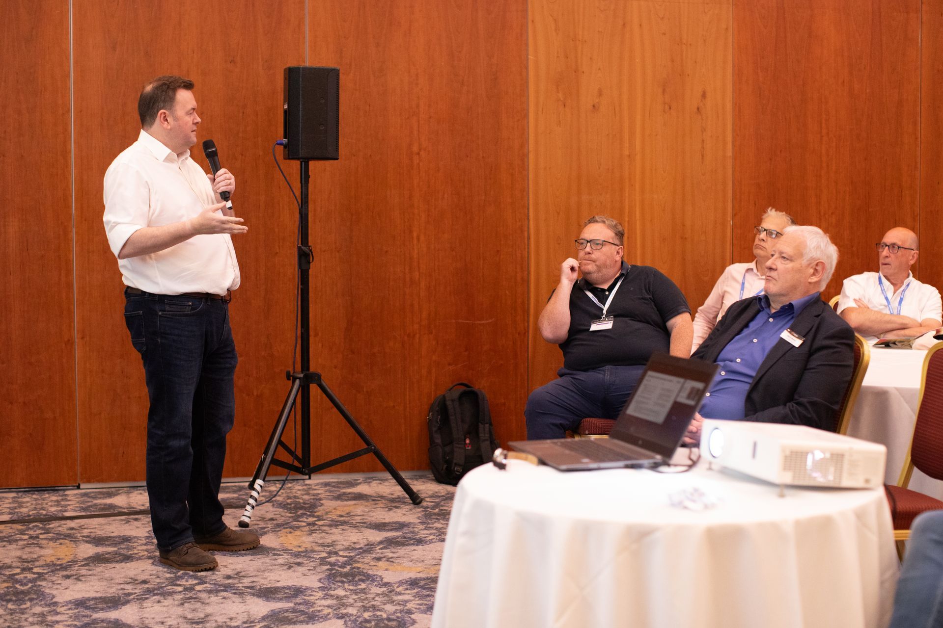 A man is giving a presentation to a group of men sitting at tables.