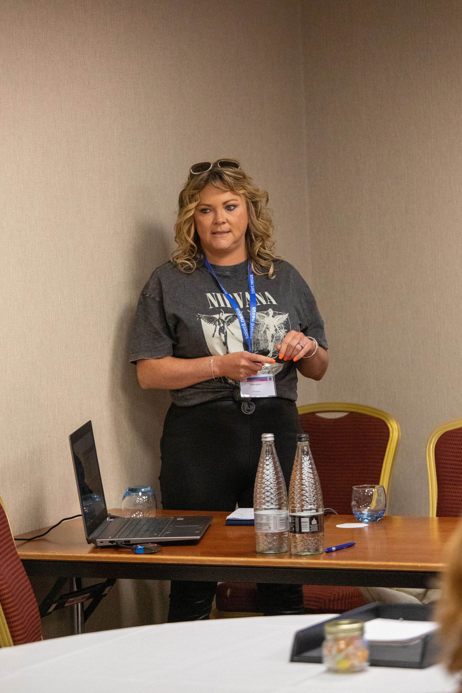 A woman is standing in front of a table with a laptop and water bottles.