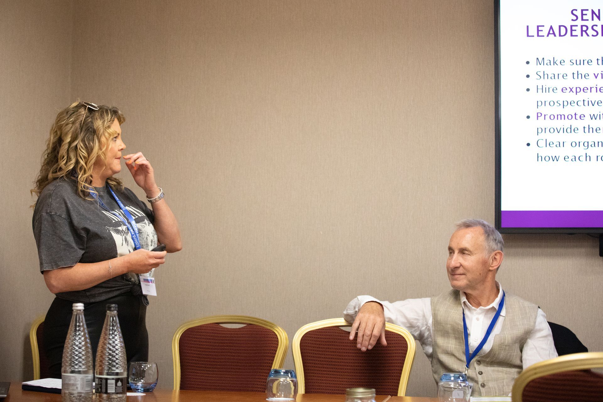 A man and a woman are sitting at a table in front of a projector screen.
