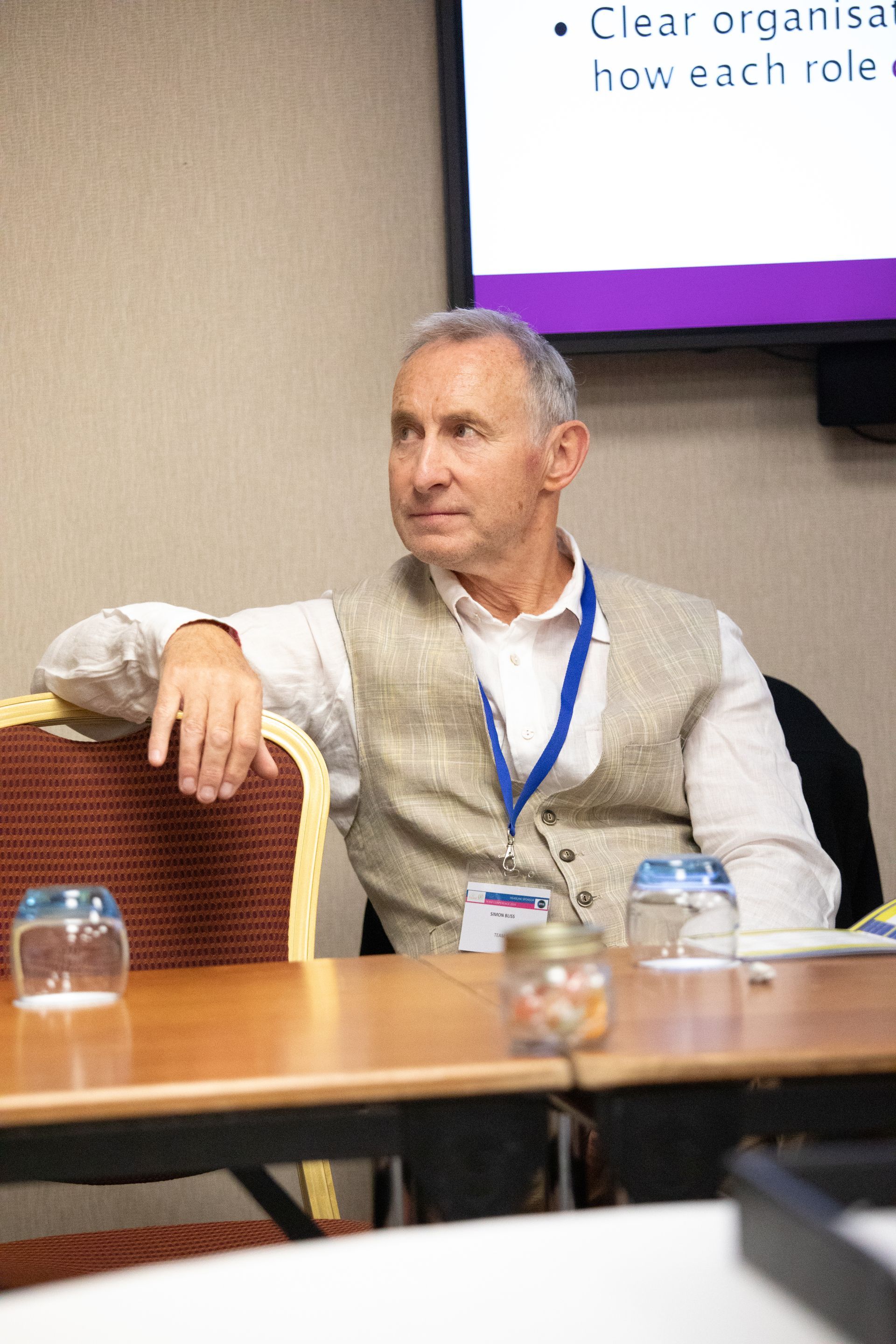 A man is sitting at a table with a name tag around his neck.