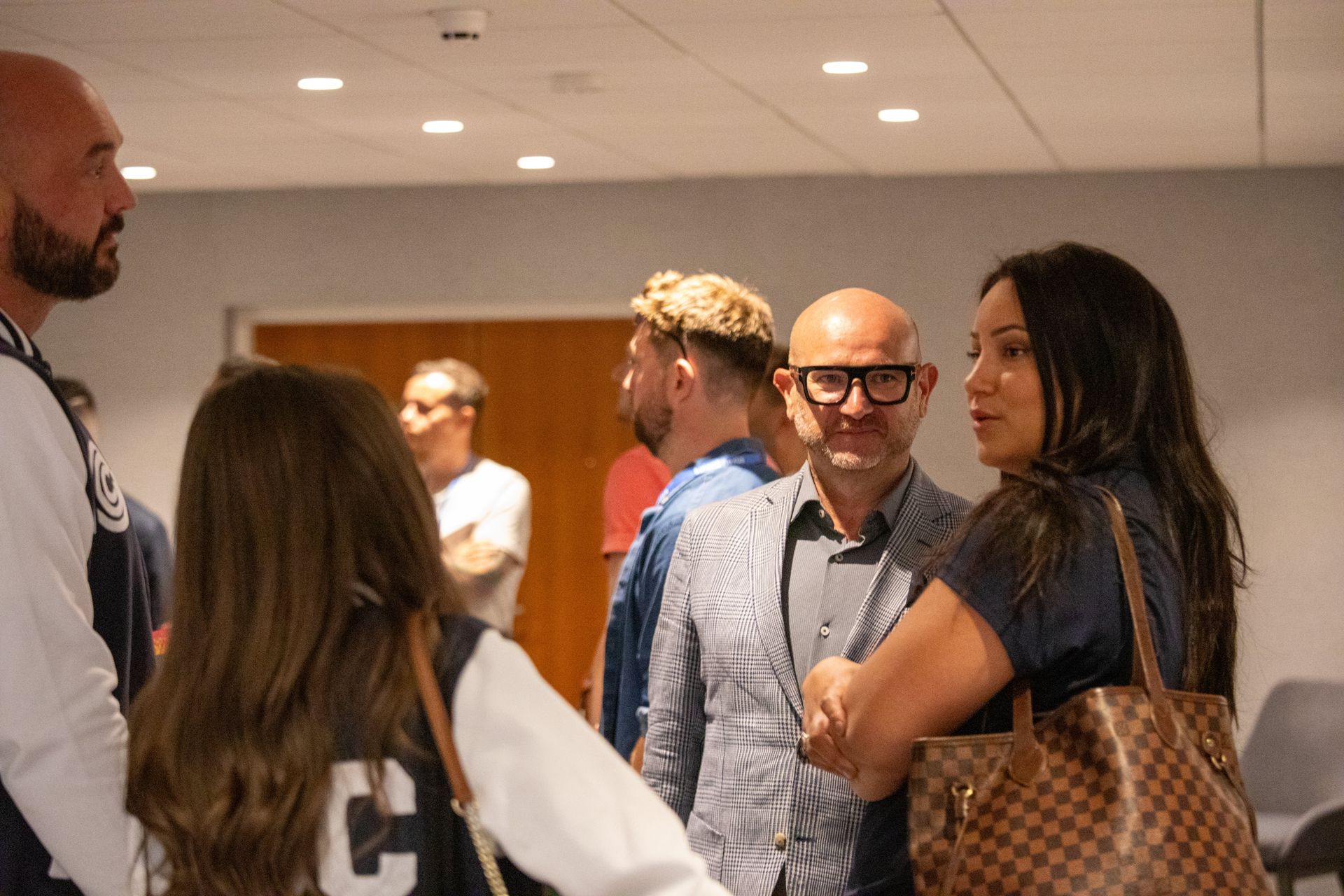 A group of people are standing in a room talking to each other.