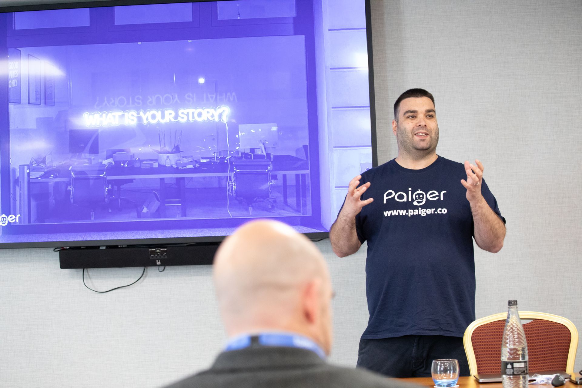 A man in a paiger shirt is giving a presentation to a group of people.
