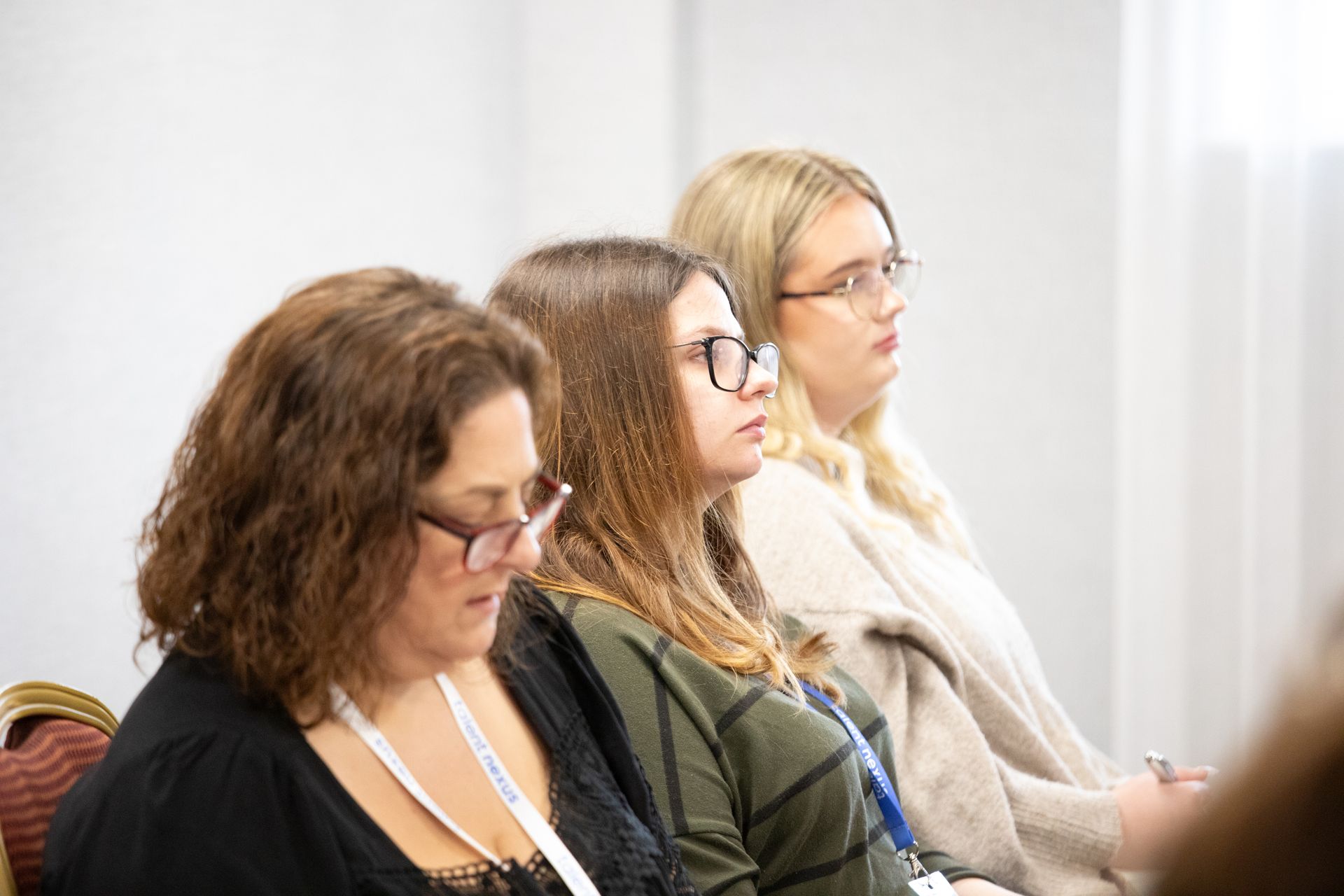 Three women wearing glasses are sitting in a row in a room.