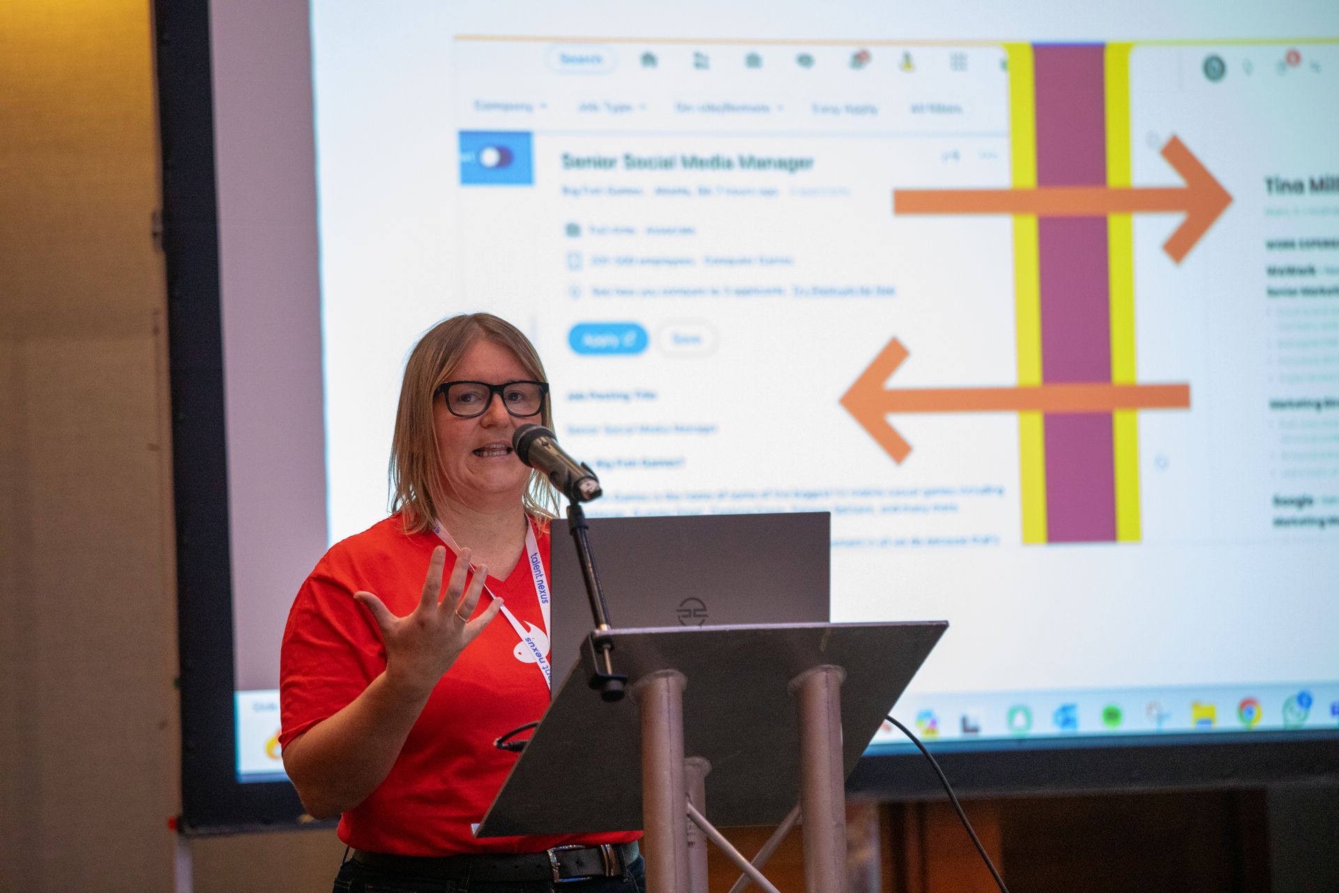 A woman is standing at a podium giving a presentation in front of a large screen.