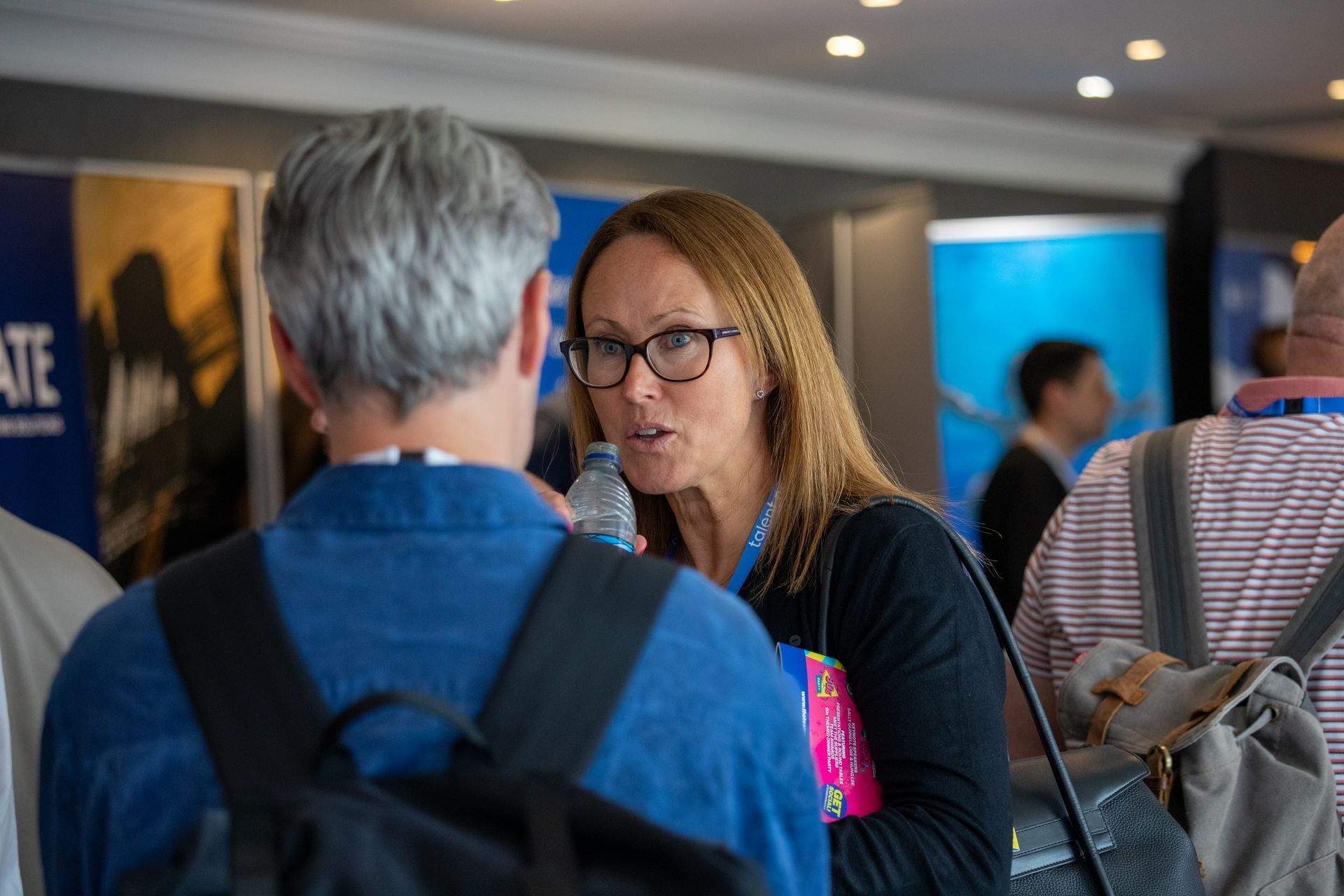 A woman is talking to a man while holding a bottle of water.