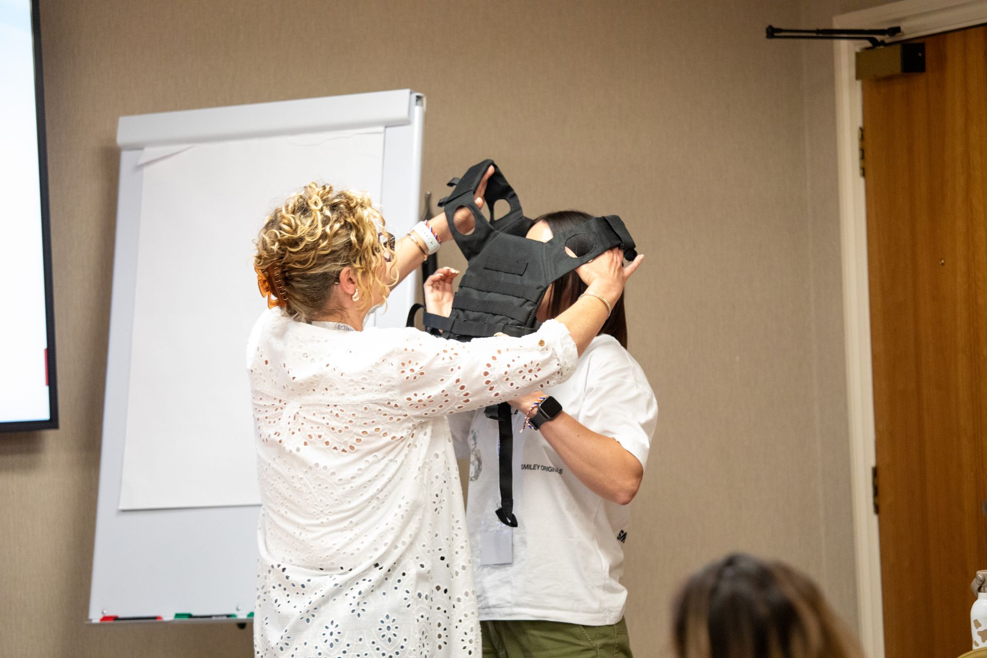A woman is putting a mask on another woman 's head.