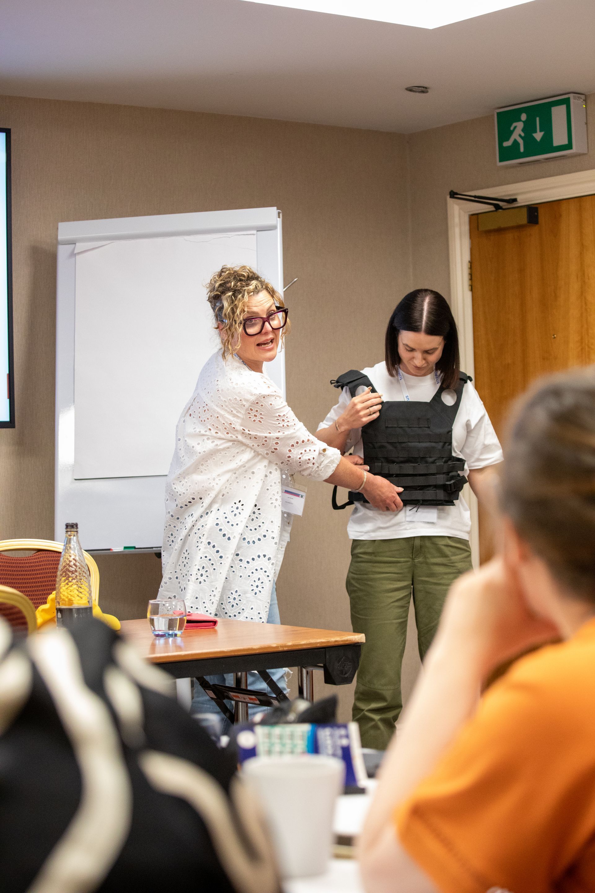A woman is helping another woman put on a bulletproof vest.