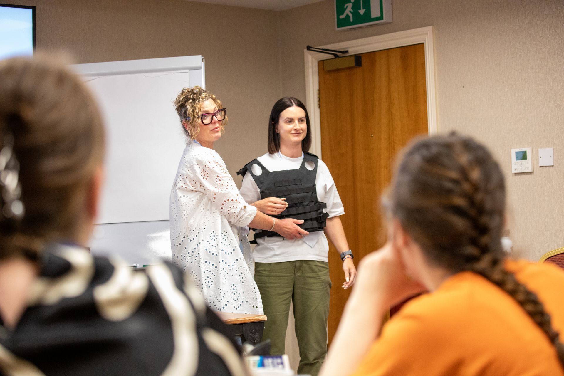 A woman is helping another woman put on a body armor.