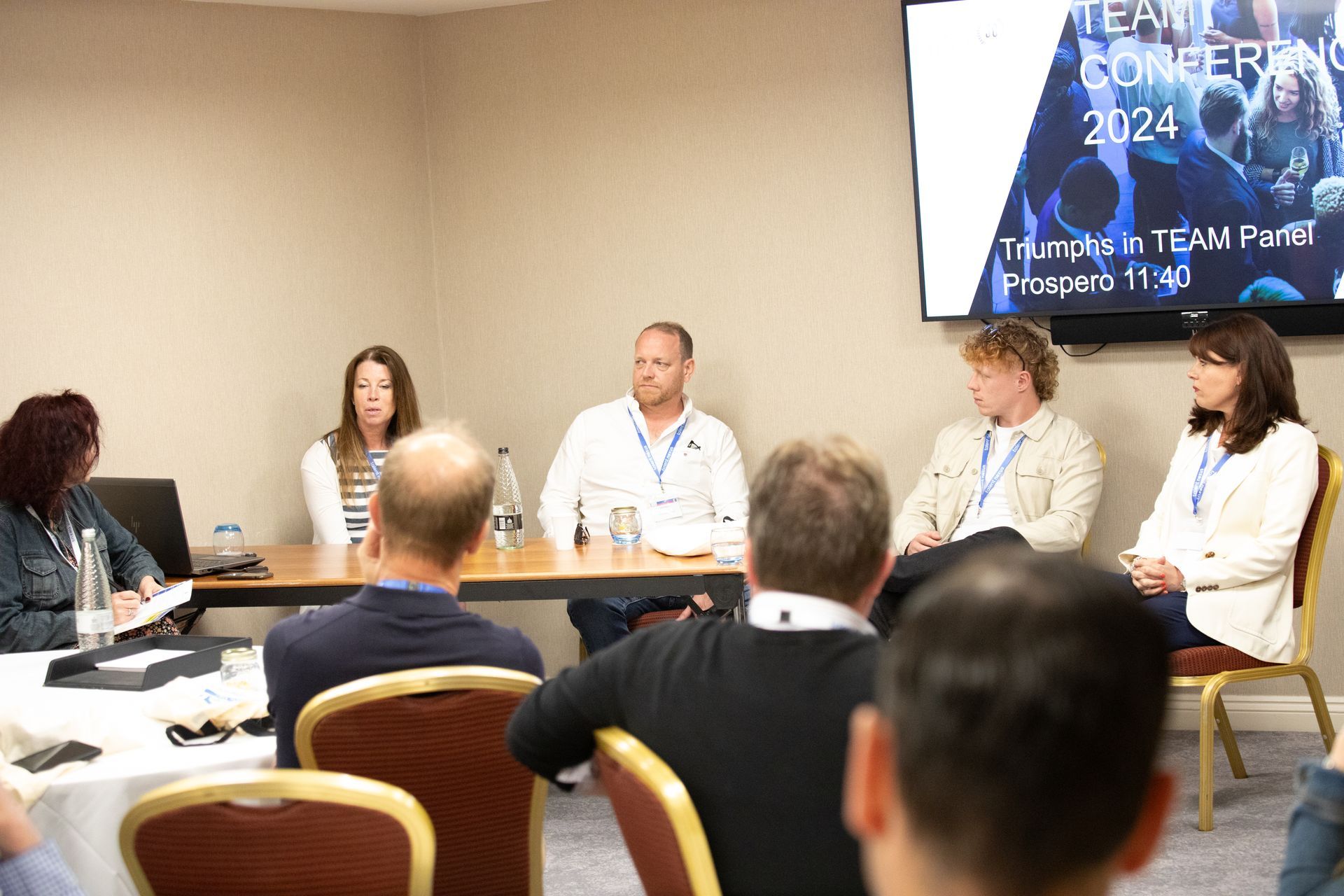 A group of people are sitting at a table in front of a large screen.