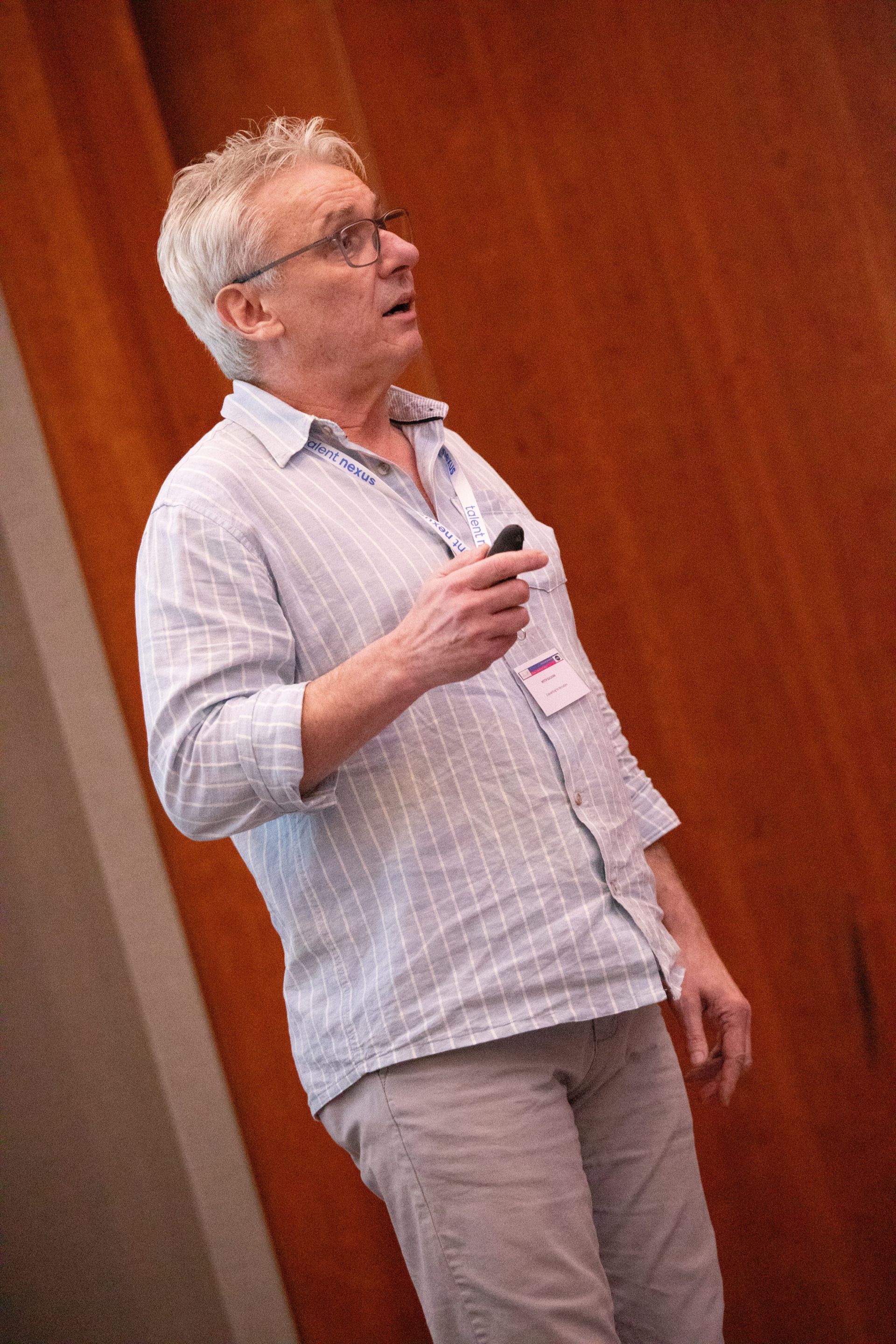 A man is standing in front of a wooden wall holding a remote control.
