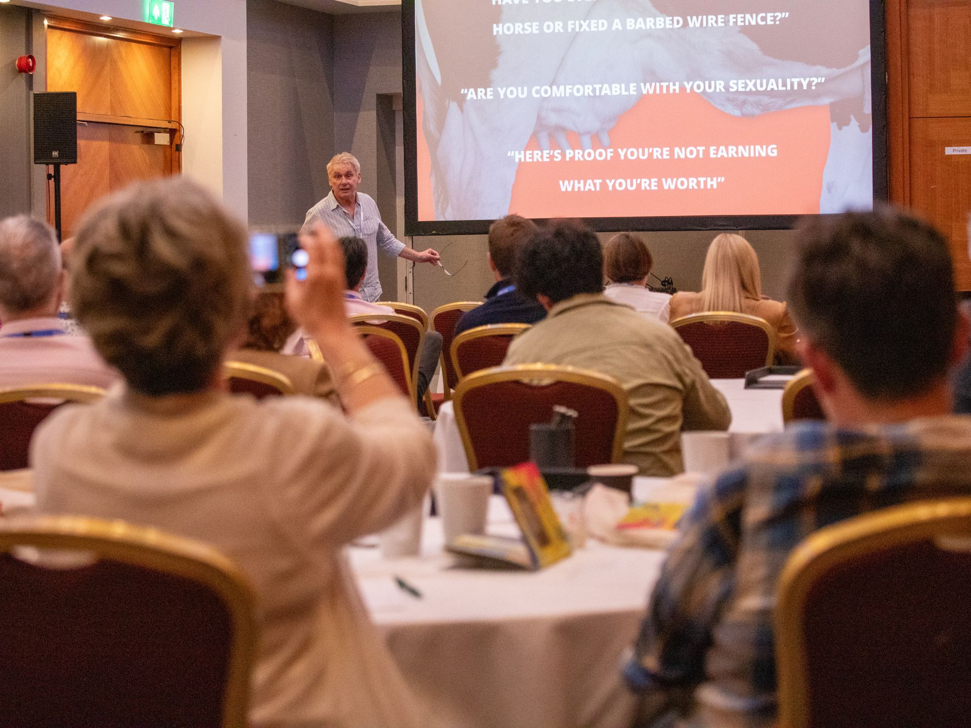 A group of people are sitting at tables in front of a large screen.