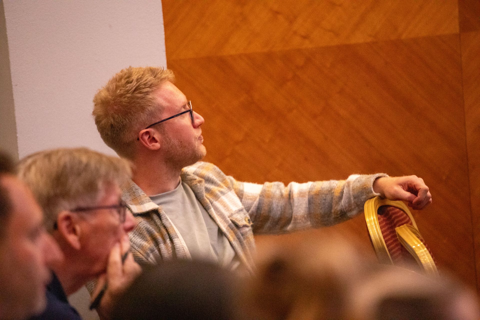 A man wearing glasses is sitting in a chair in front of a group of people.