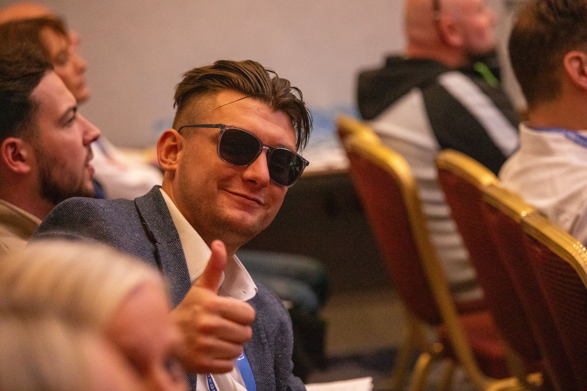 A man wearing sunglasses is giving a thumbs up while sitting in a chair.