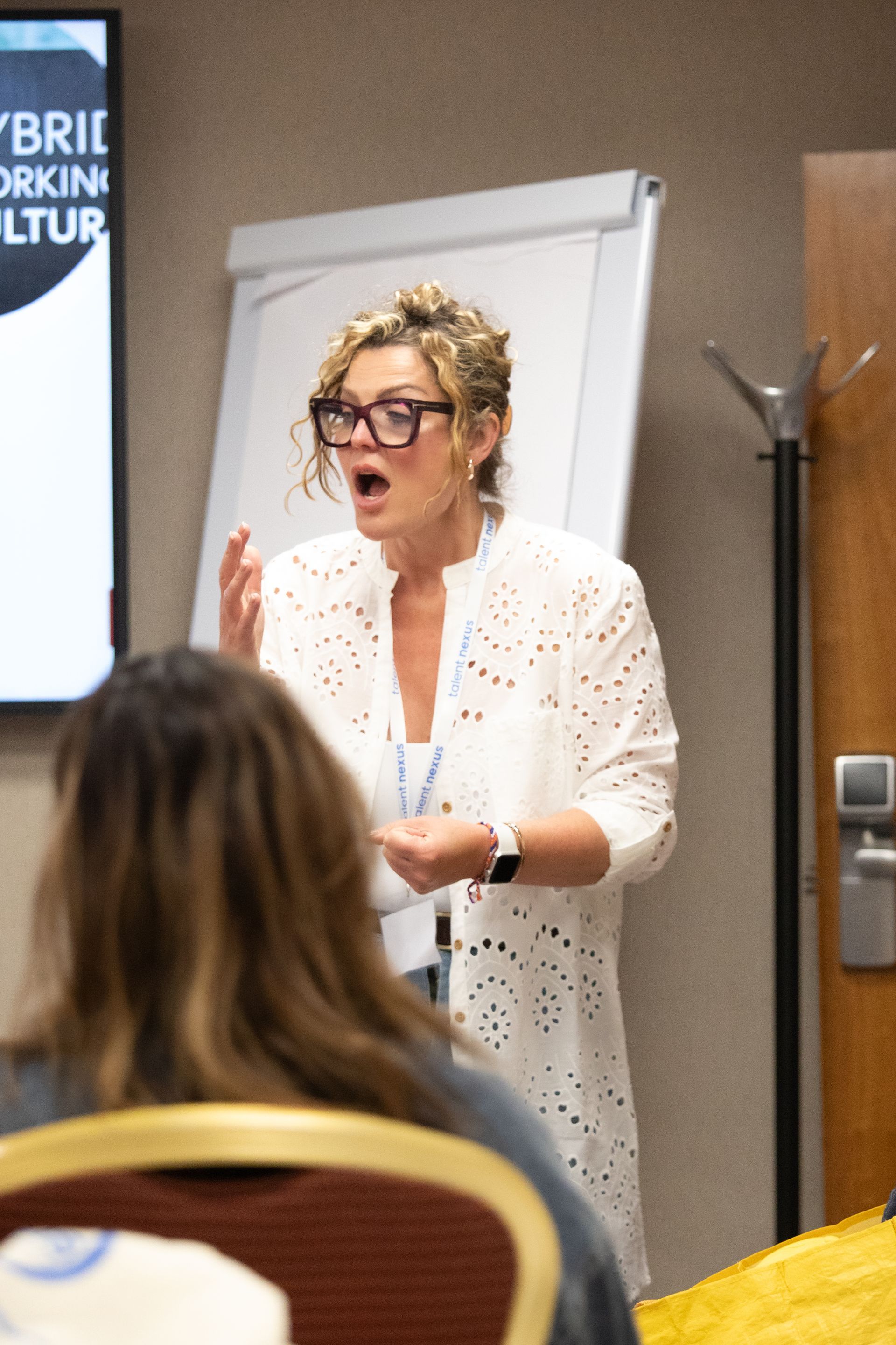 A woman wearing glasses is giving a presentation to a group of people