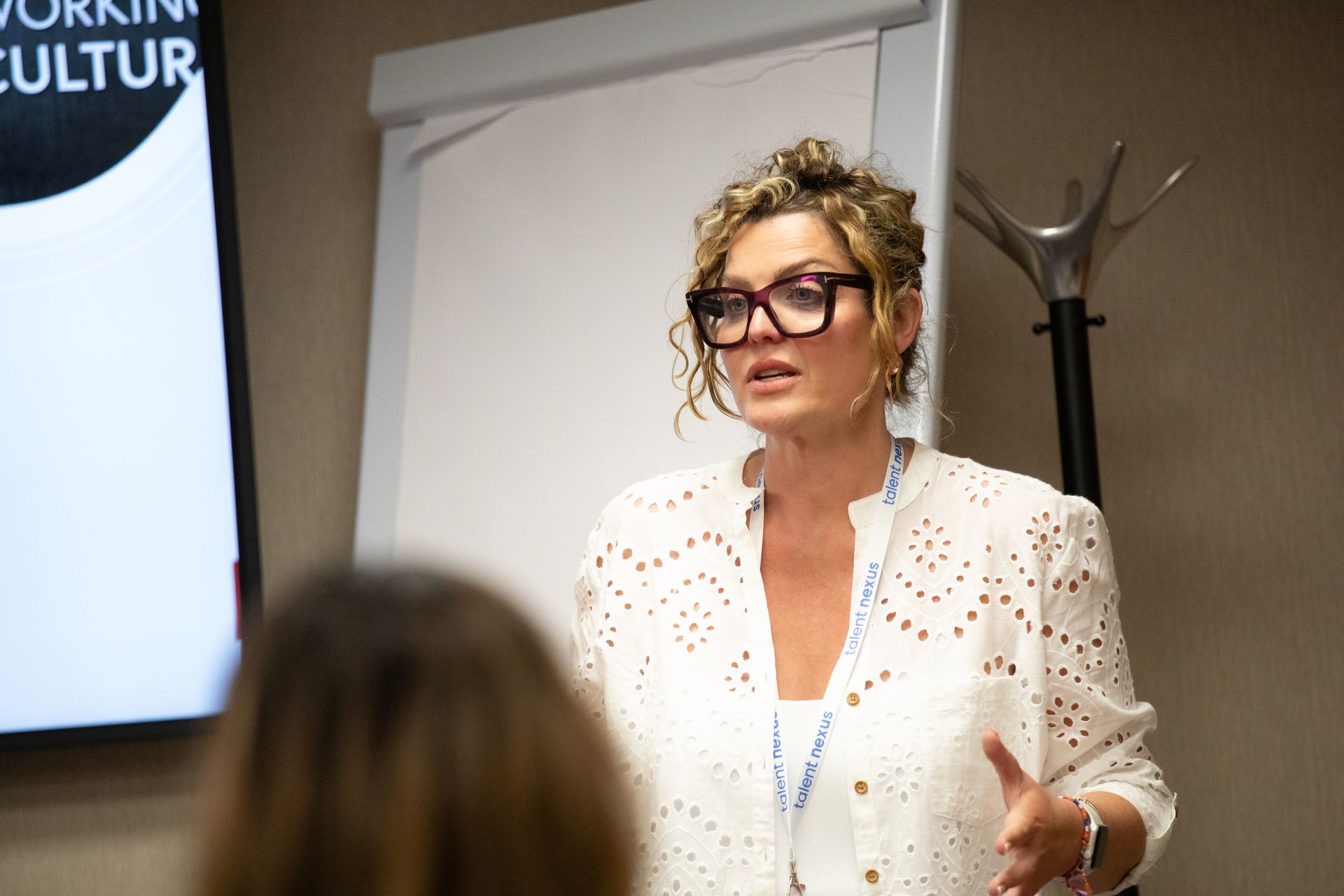 A woman wearing glasses is giving a presentation to a group of people.