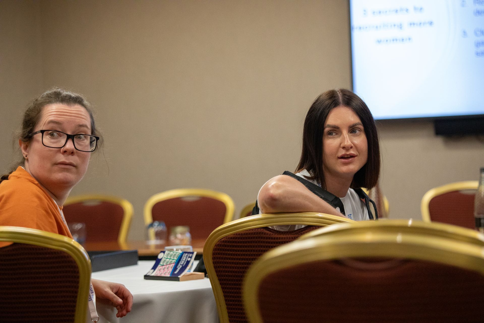 Two women are sitting at a table in a conference room.