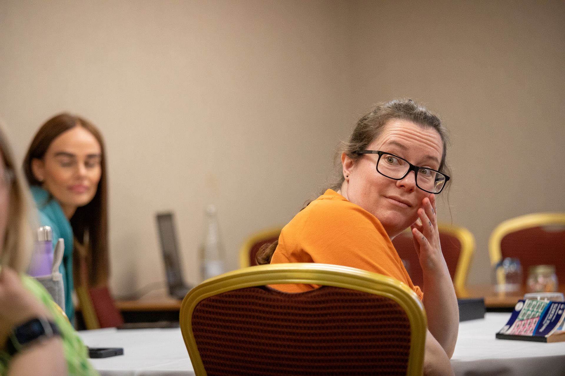 A woman wearing glasses is sitting at a table with other people.