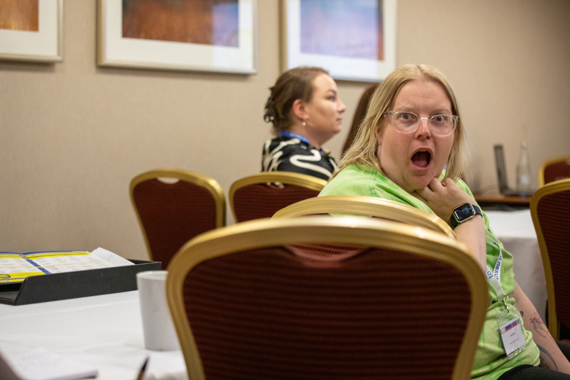 A woman is sitting at a table with a surprised look on her face.