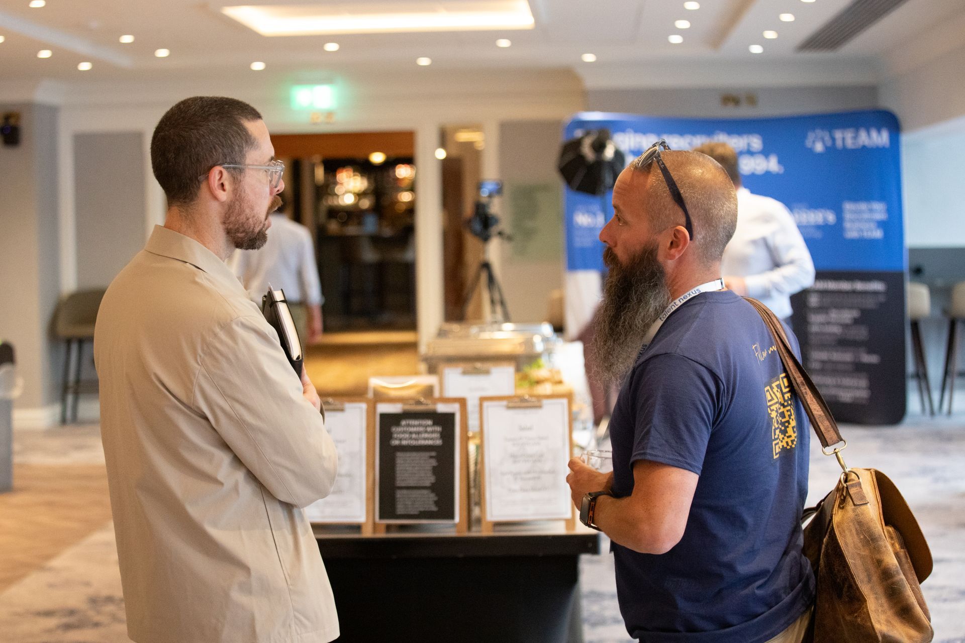 Two men are standing next to each other in a room talking to each other.
