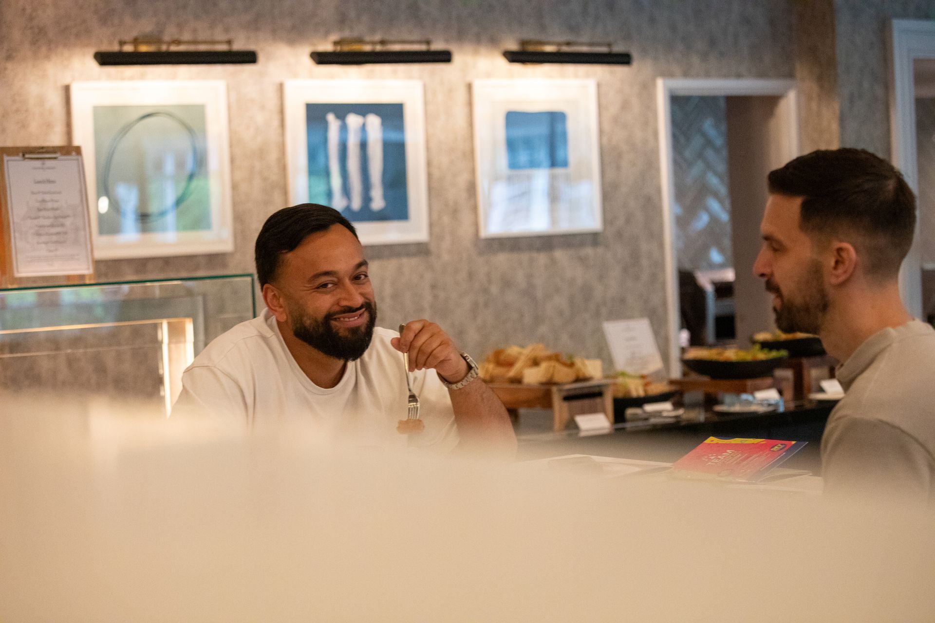 Two men are sitting at a table in a restaurant talking to each other.