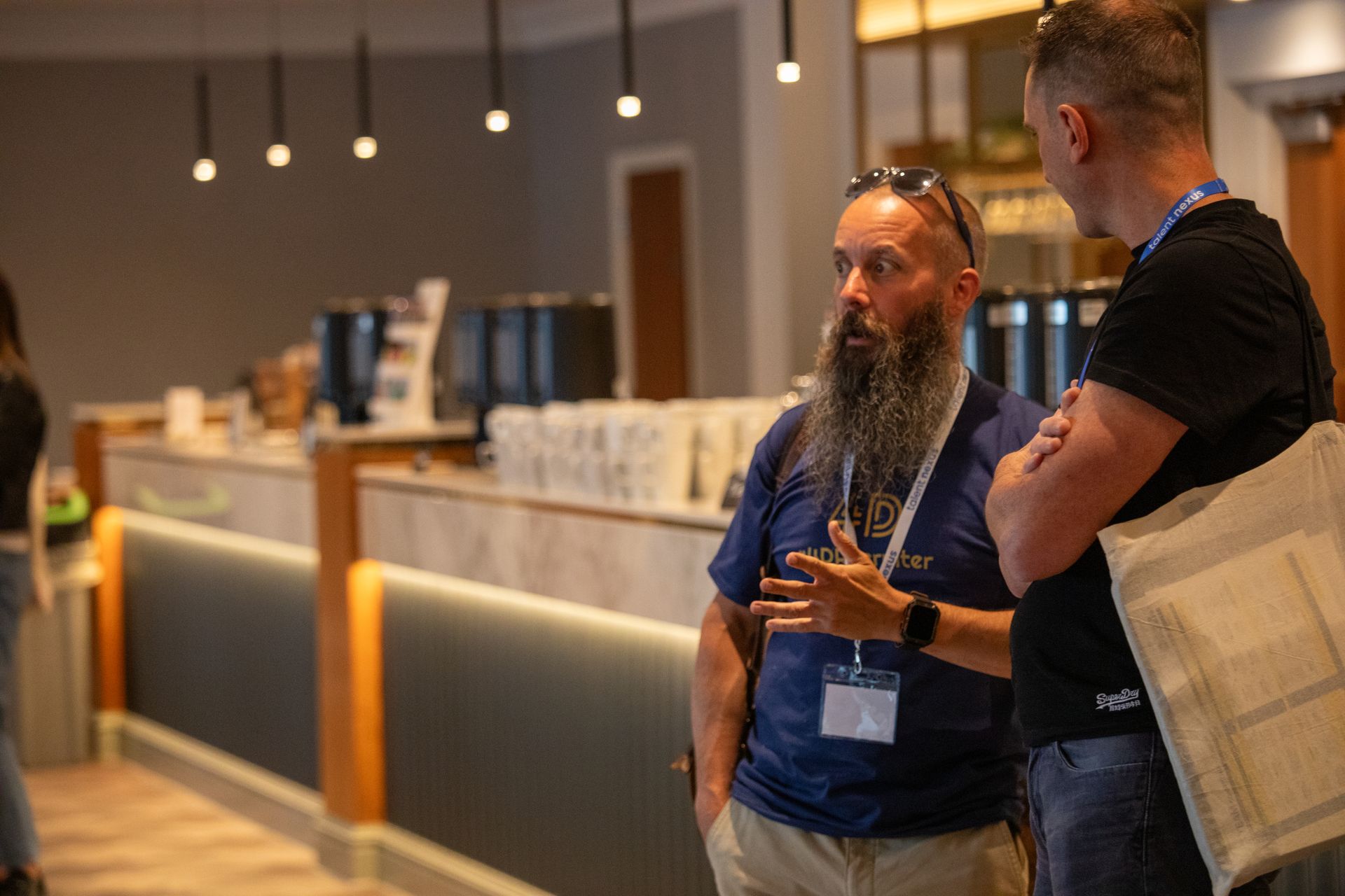 A man with a beard is talking to another man in a restaurant.
