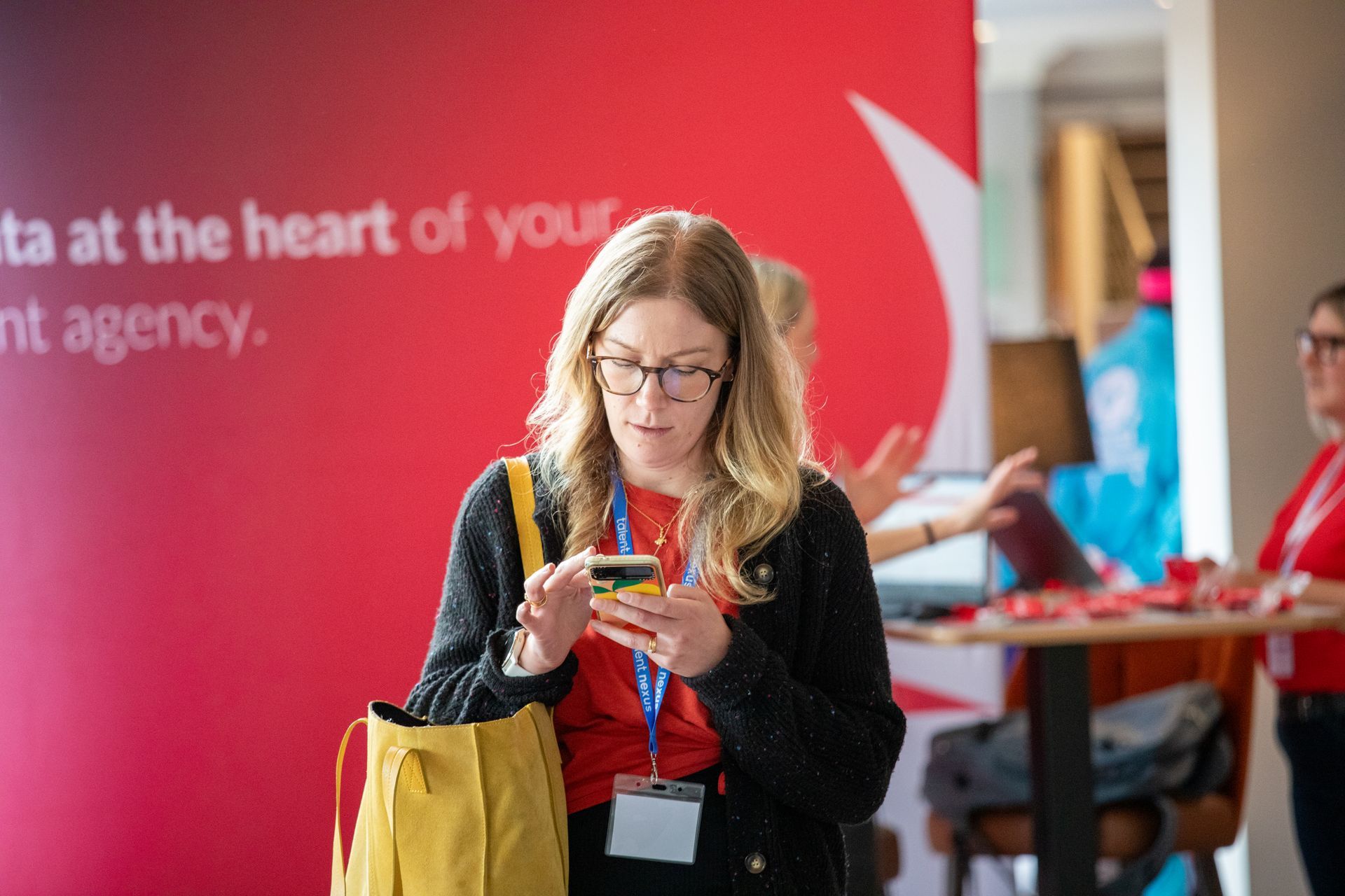 A woman is standing in front of a red wall looking at her phone.