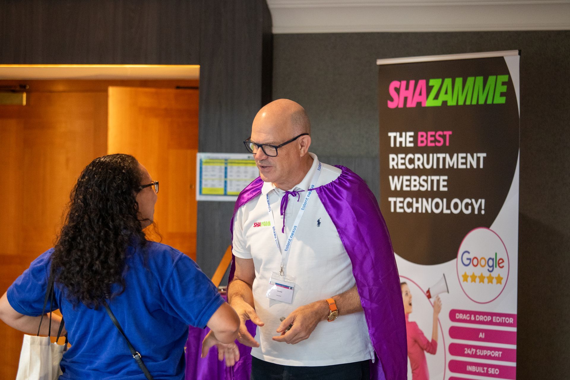 A man in a purple cape is standing next to a woman in a blue shirt.