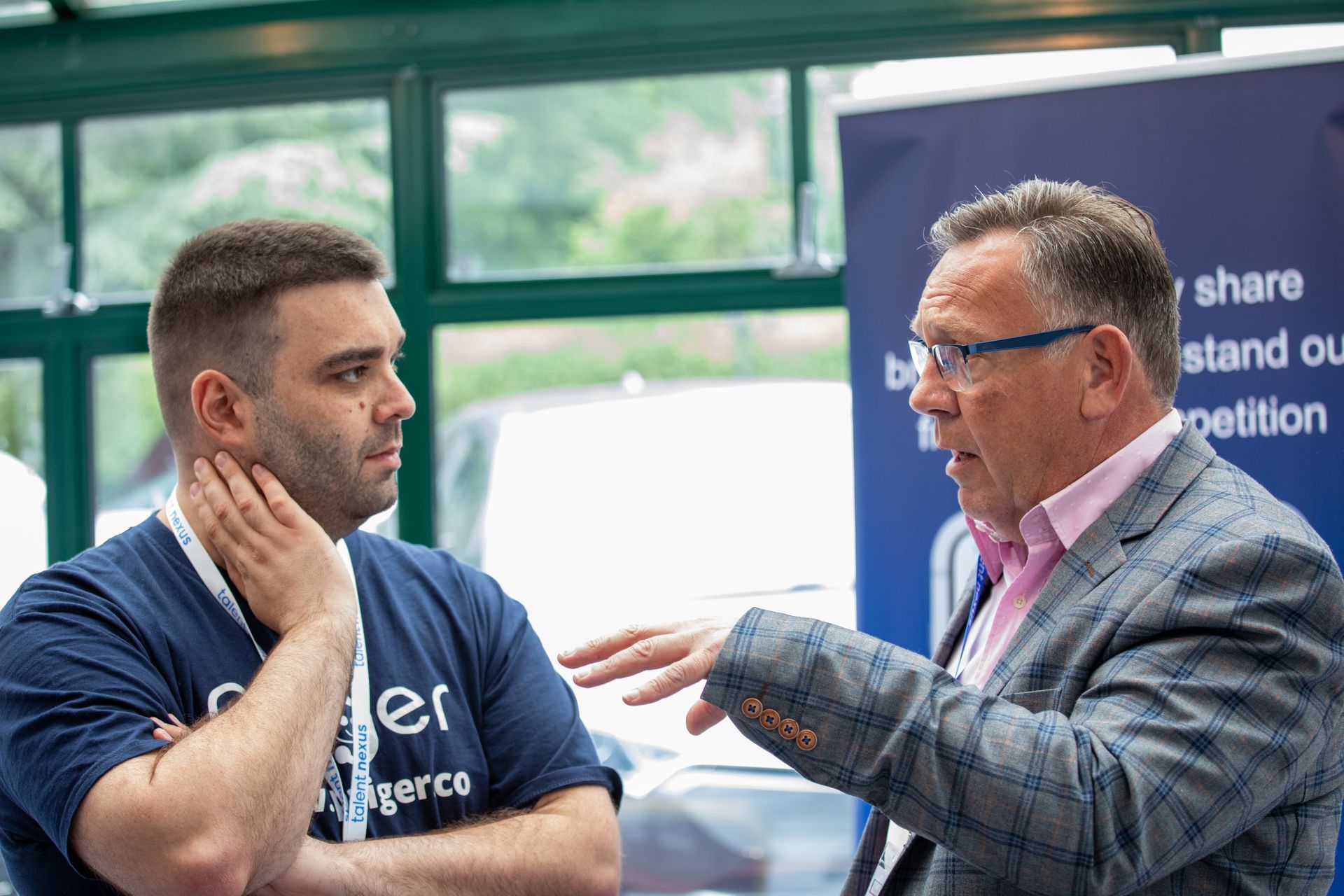 Two men are talking to each other in front of a window.
