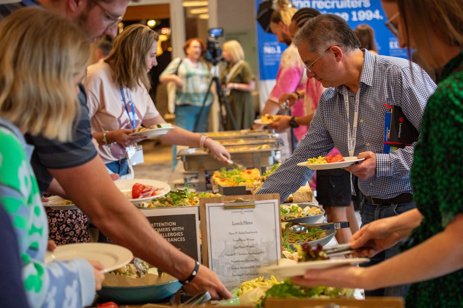 A group of people are standing around a buffet table eating food.