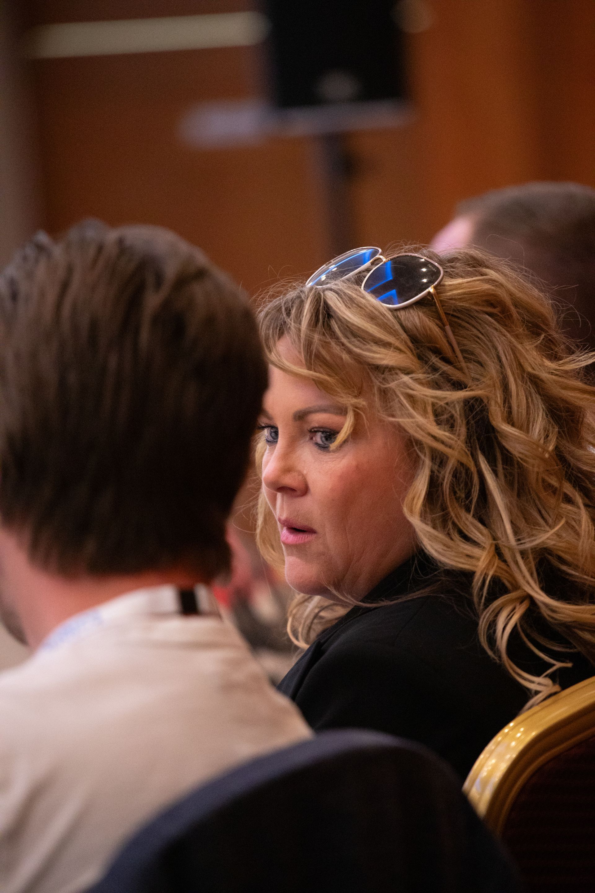 A woman wearing sunglasses is sitting in a chair talking to a man.